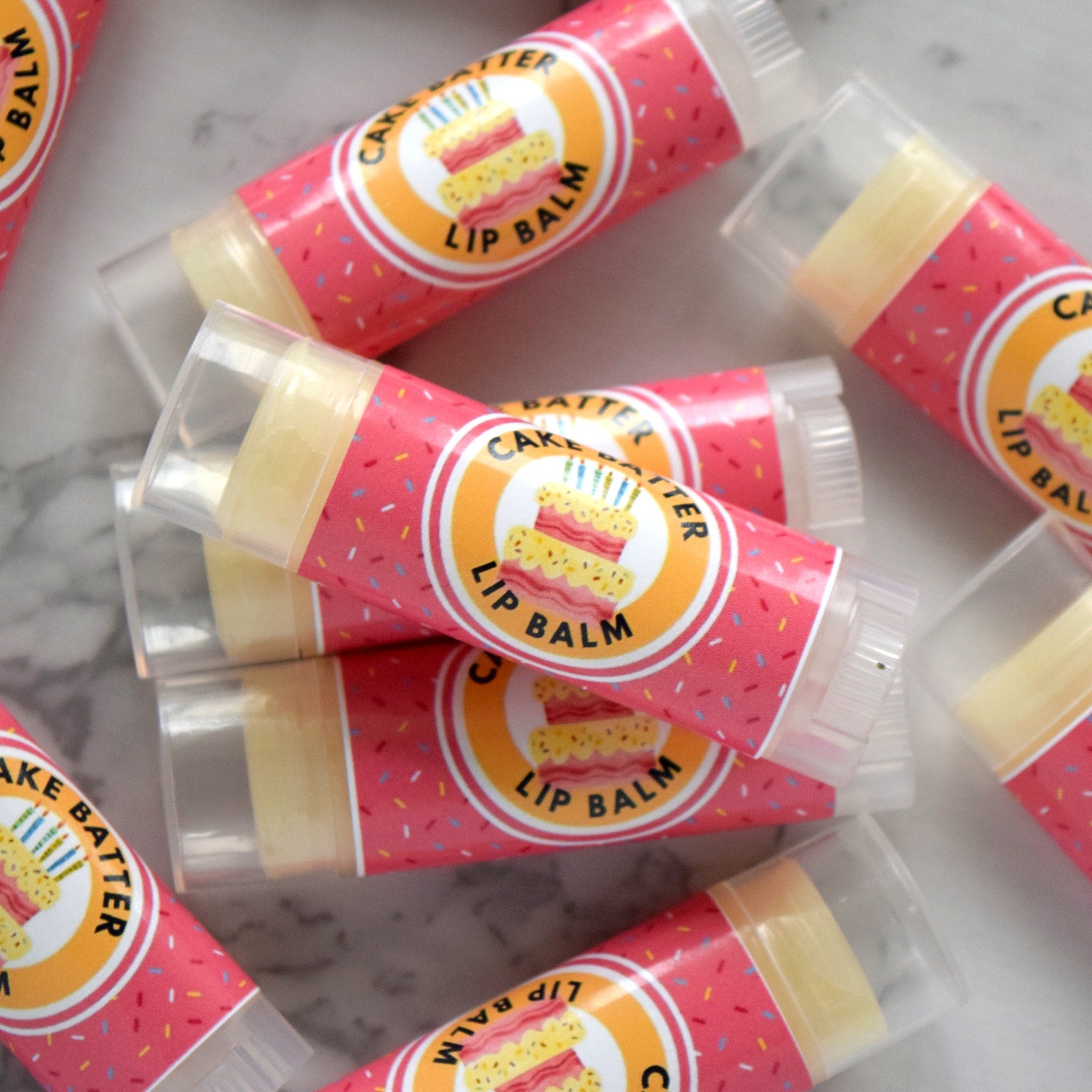 Lip balm tubes with pink and confetti pattern, clear plastic cap, and "Cake Batter Lip Balm" label