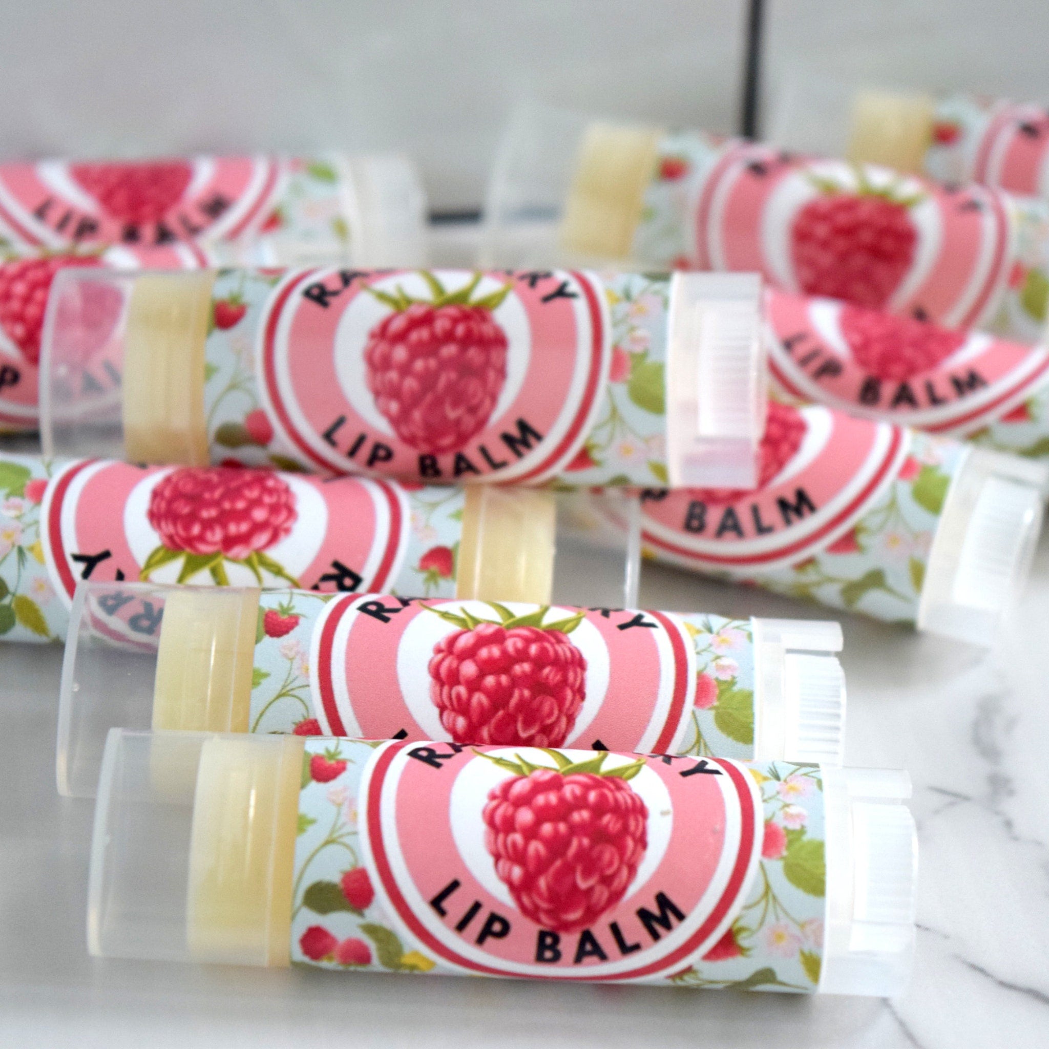 Lip balm tubes with pink, white, and floral pattern labels, clear plastic caps, and visible product
