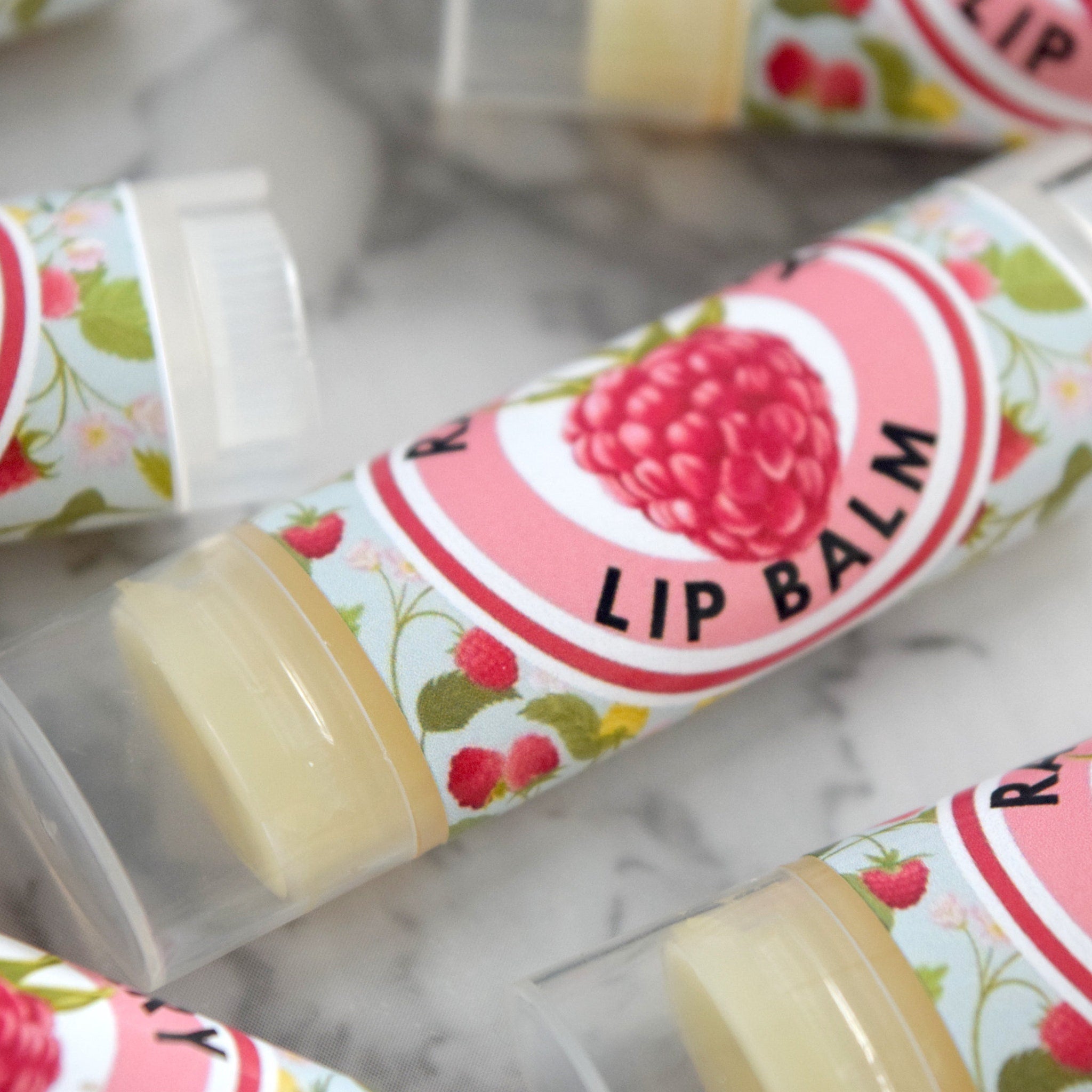Lip balm tubes with pink and floral patterned labels, clear plastic casing, and visible product inside