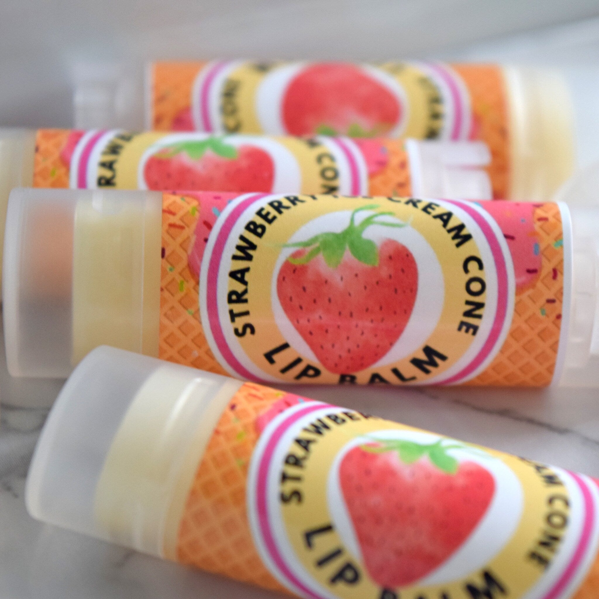 Lip balm tubes with strawberry labels, orange waffle cone pattern, and clear caps