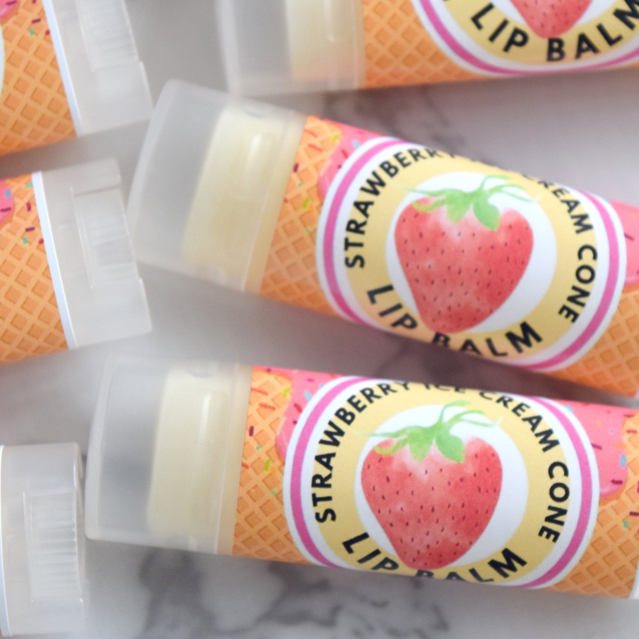 Lip balm tubes with strawberry design, orange waffle cone pattern, and clear caps
