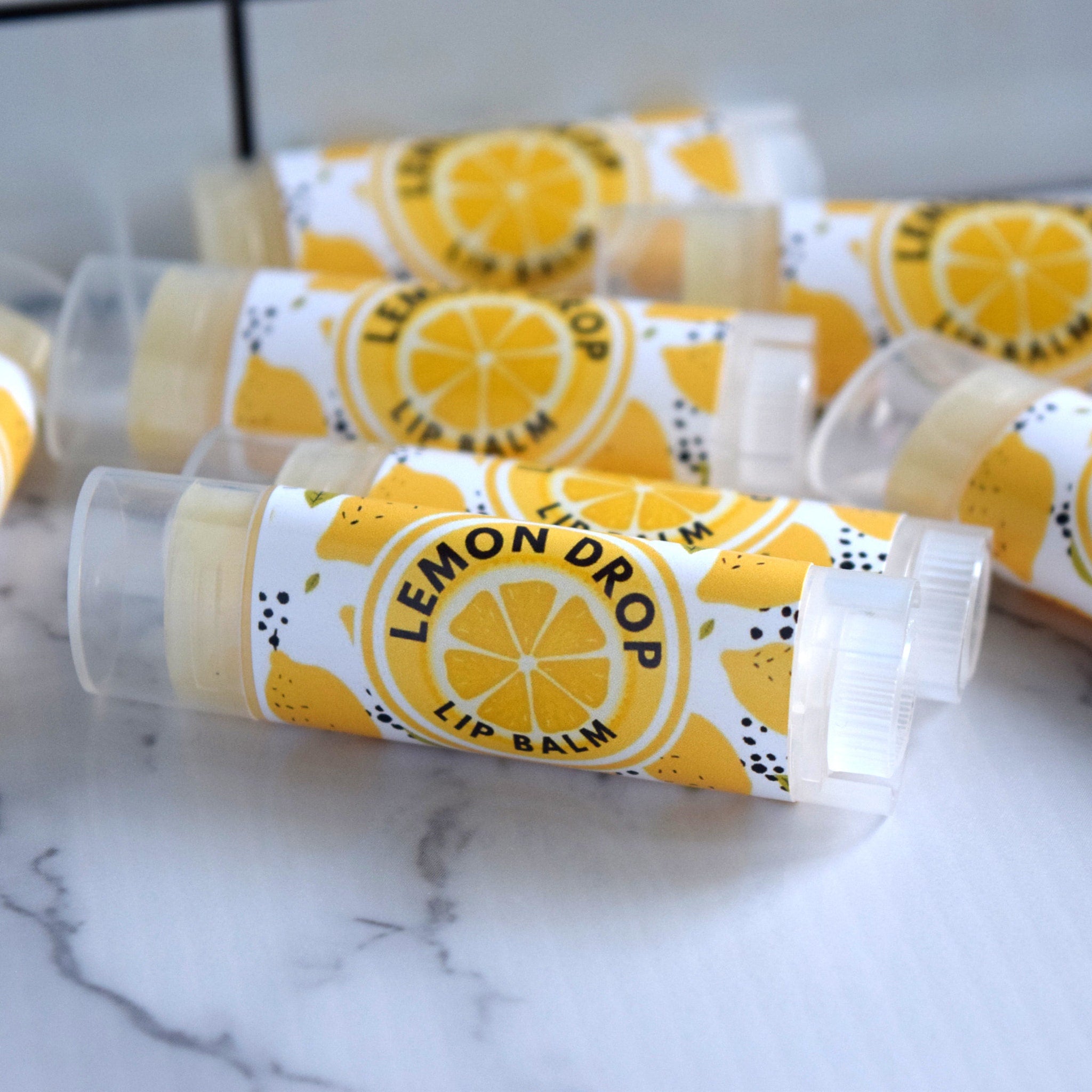 Lip balm tubes with yellow and white labels, clear plastic caps, and "Lemon Drop" text