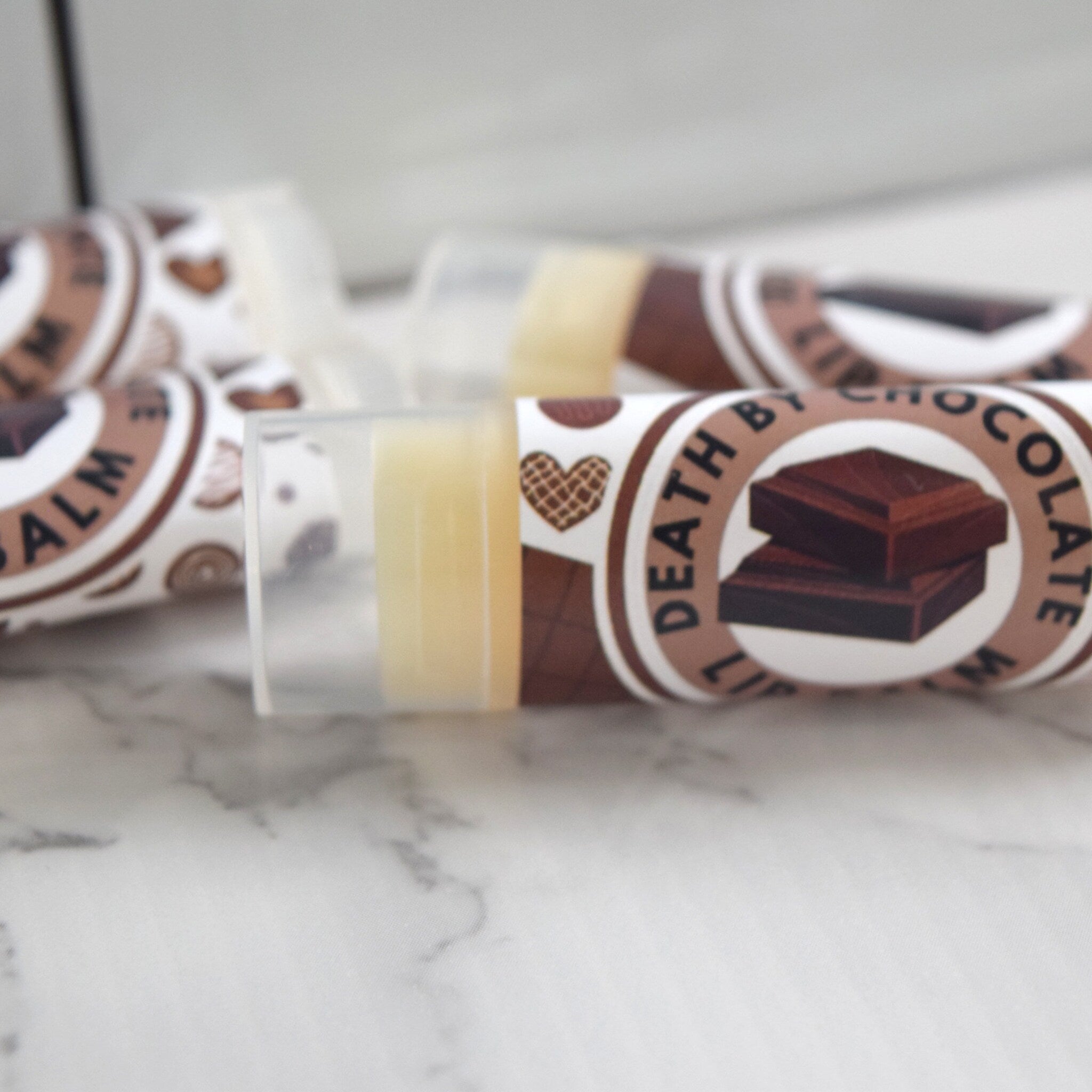 Lip balm tubes with brown and white label, clear plastic cap, and "Death By Chocolate" text