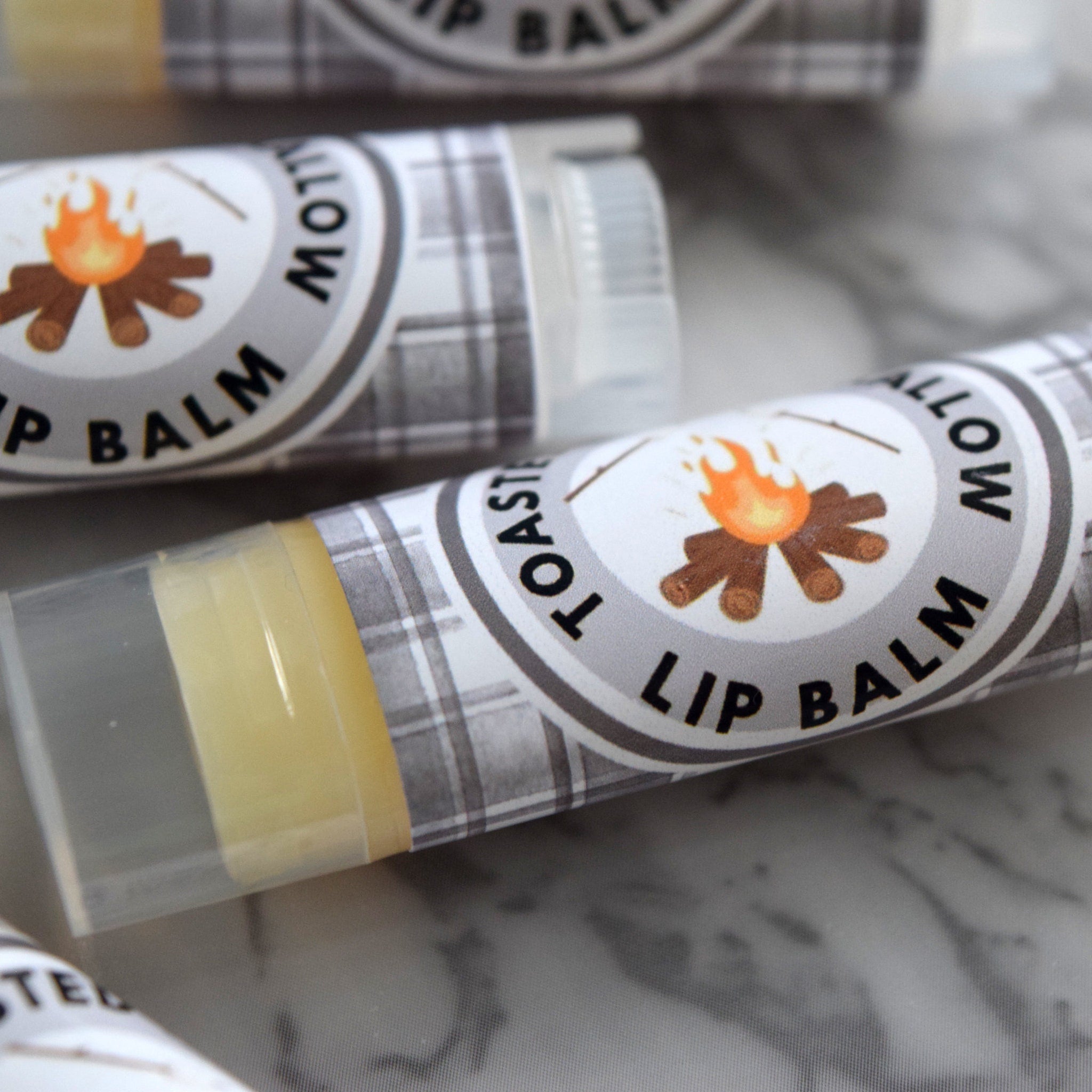Lip balm tubes with plaid pattern, clear plastic, and campfire illustration