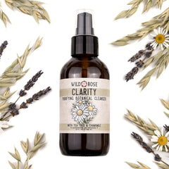 Facial cleanser bottle, brown glass with pump, Wild Rose Clarity label, surrounded by botanicals