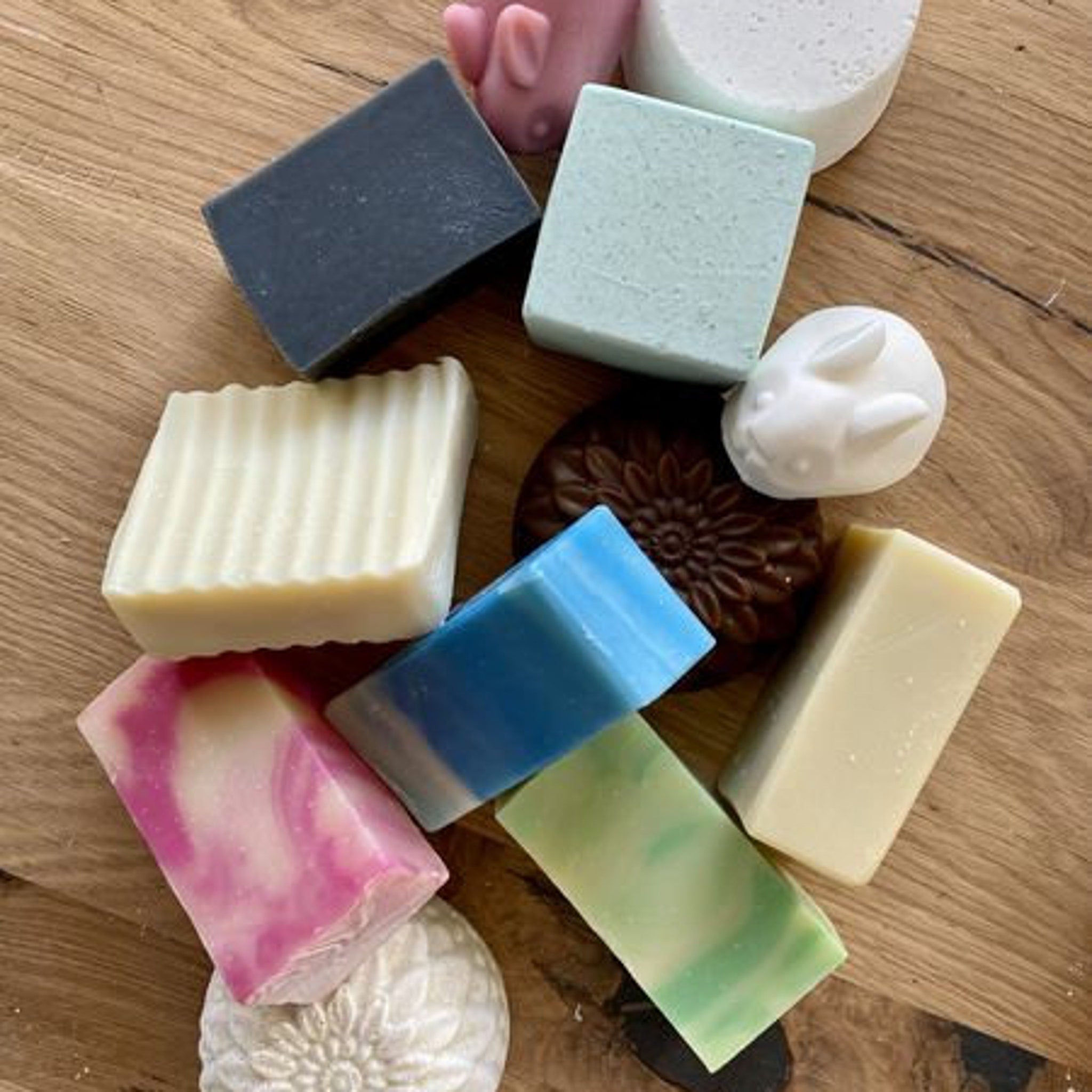 Soaps in various colors and shapes, including blue, green, and white bars, on wooden surface