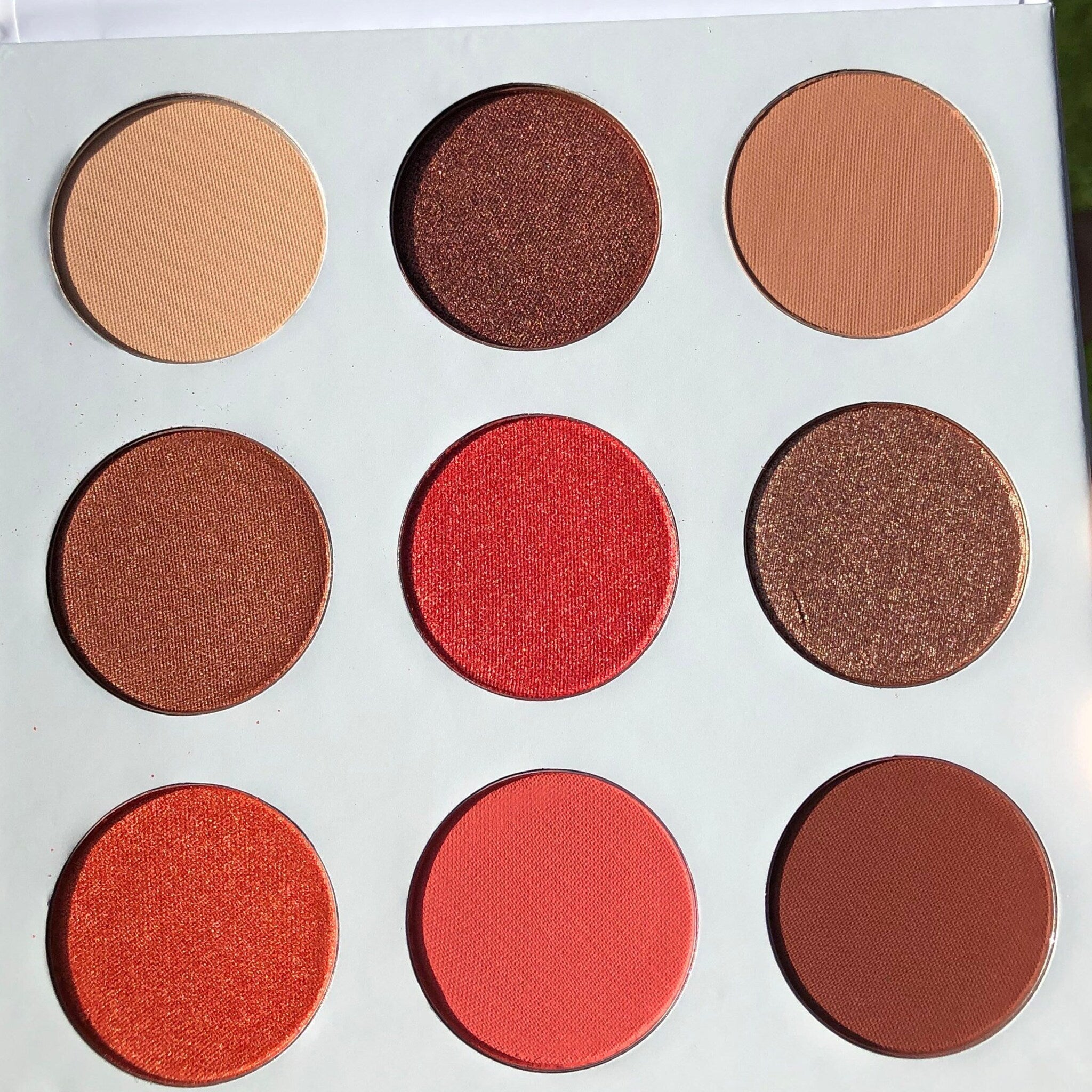 Close-up of fingertips applying shimmery red and pink eye shadow from daisy-shaped palette