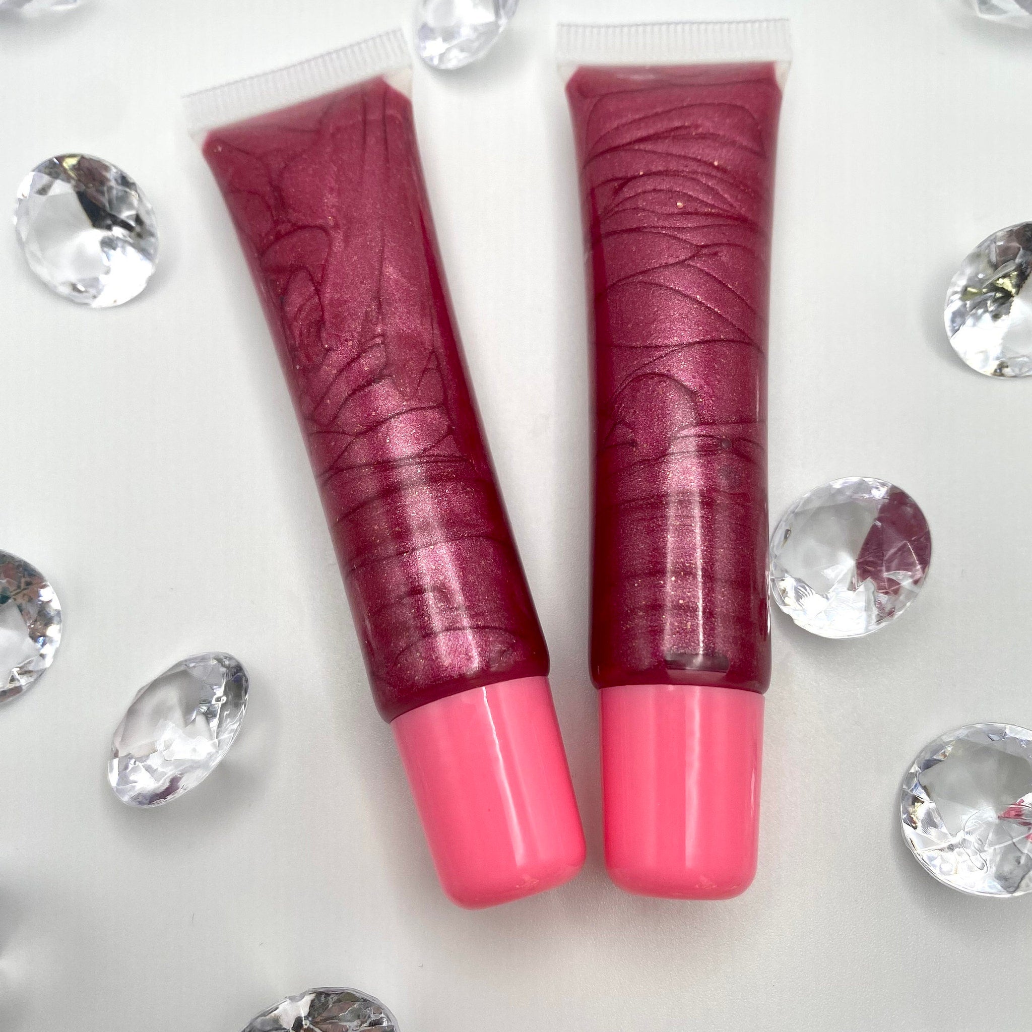 Lip gloss tubes with shimmery burgundy gloss and pink base, on white background with crystals