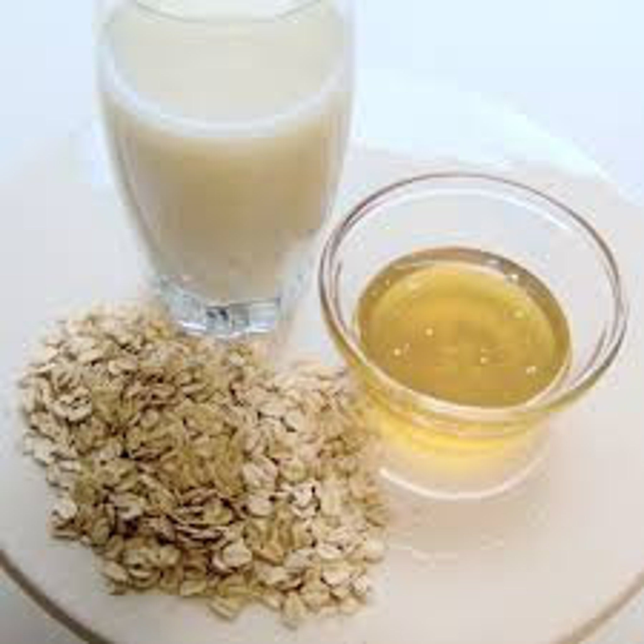 Oatmeal and honey ingredients with glass of liquid, beige oats, clear glass bowl, and yellow liquid