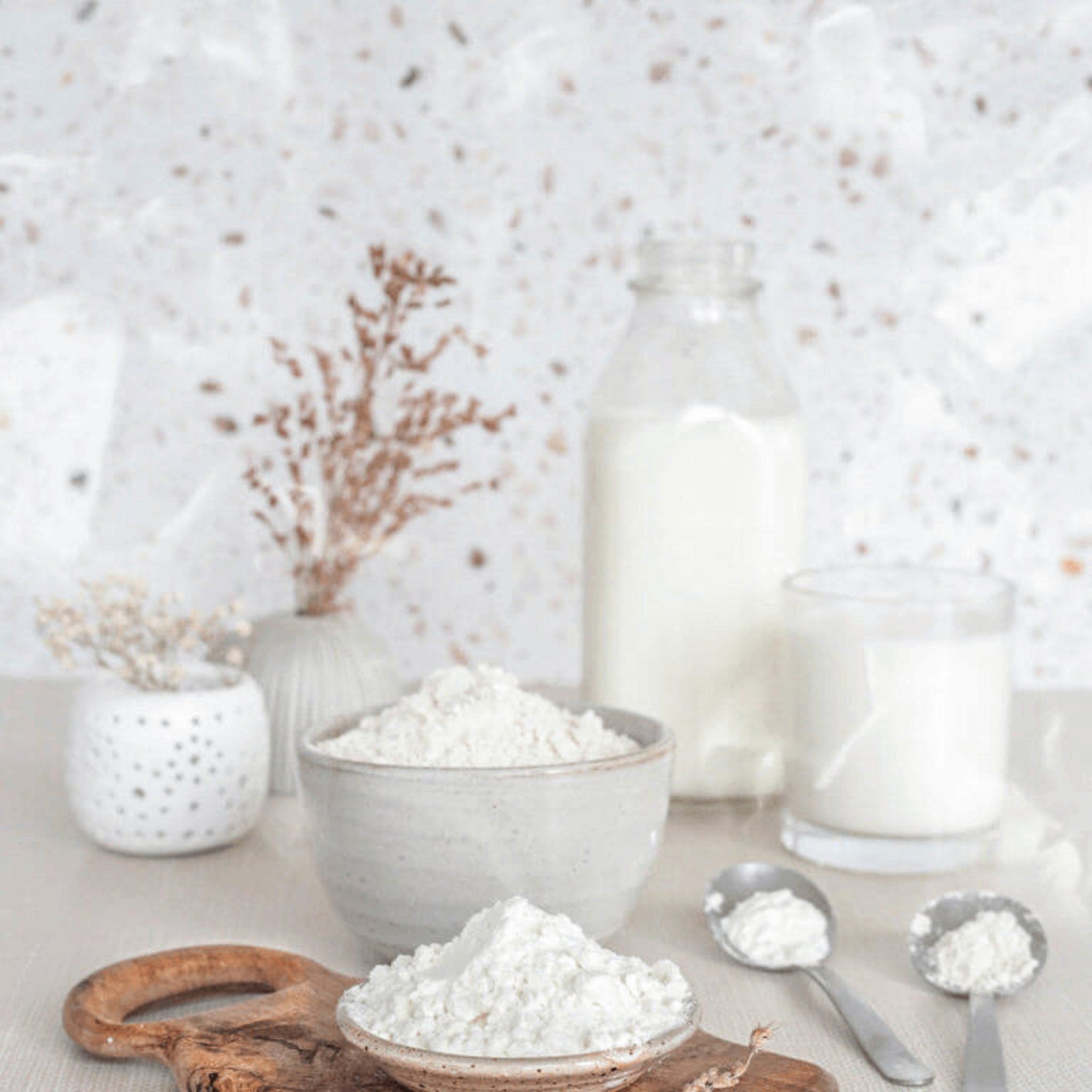Flour in white ceramic bowls with wooden cutting board and milk in glass bottle and cup