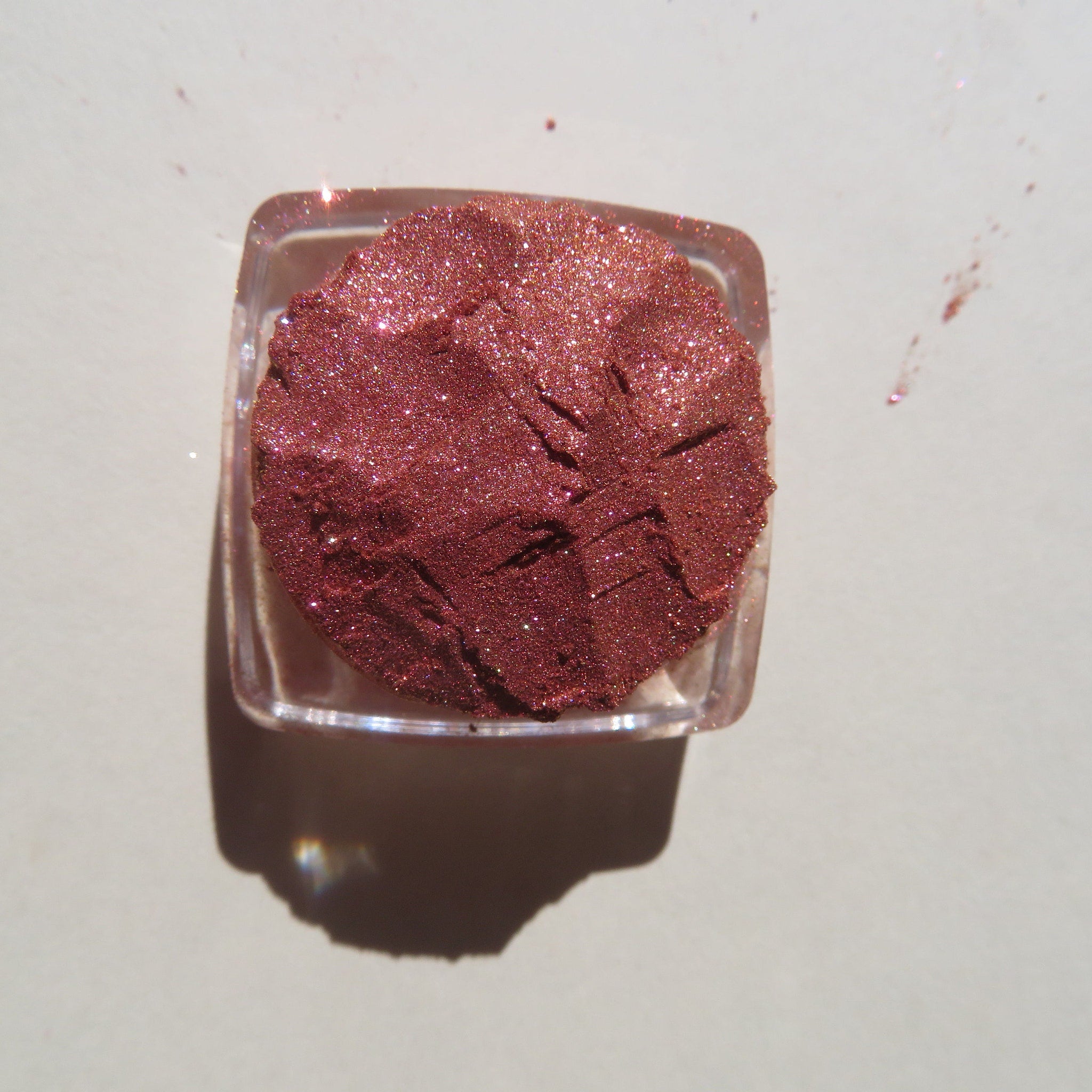 Close-up of shimmering loose pigment eye shadow in orange-pink-gold tones with metallic finish