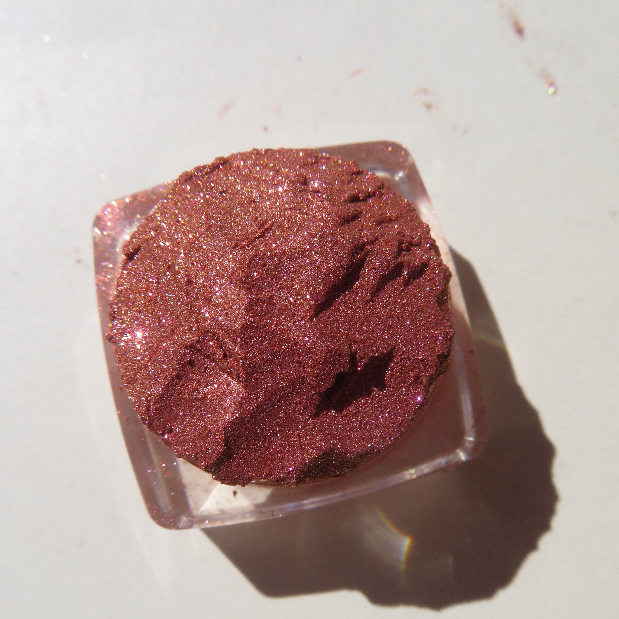 Hand applying shimmering orange-pink-gold vegan loose eye shadow pigment with fingertip