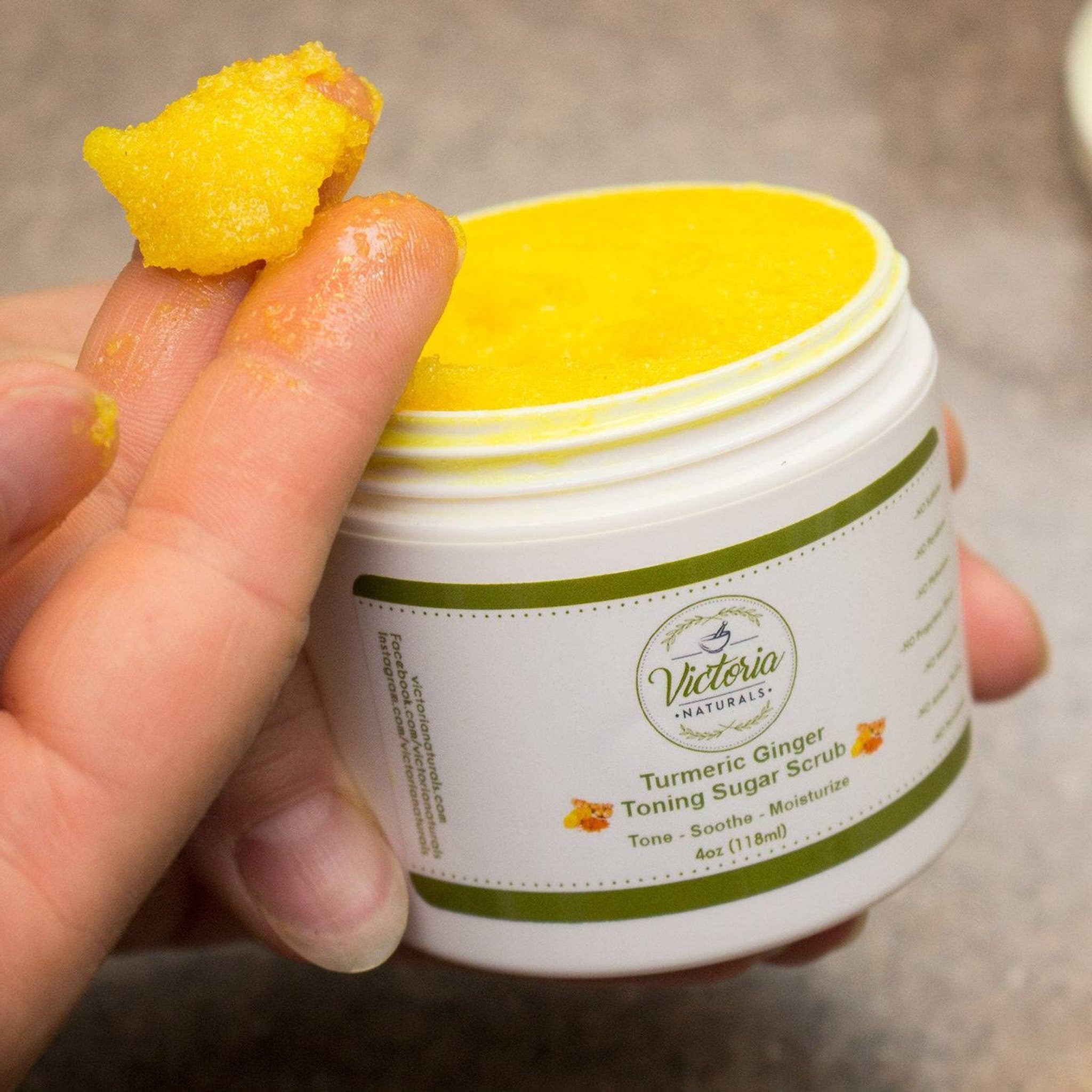 Toning sugar scrub with yellow granules, white jar, and Victoria Naturals branding on a hand