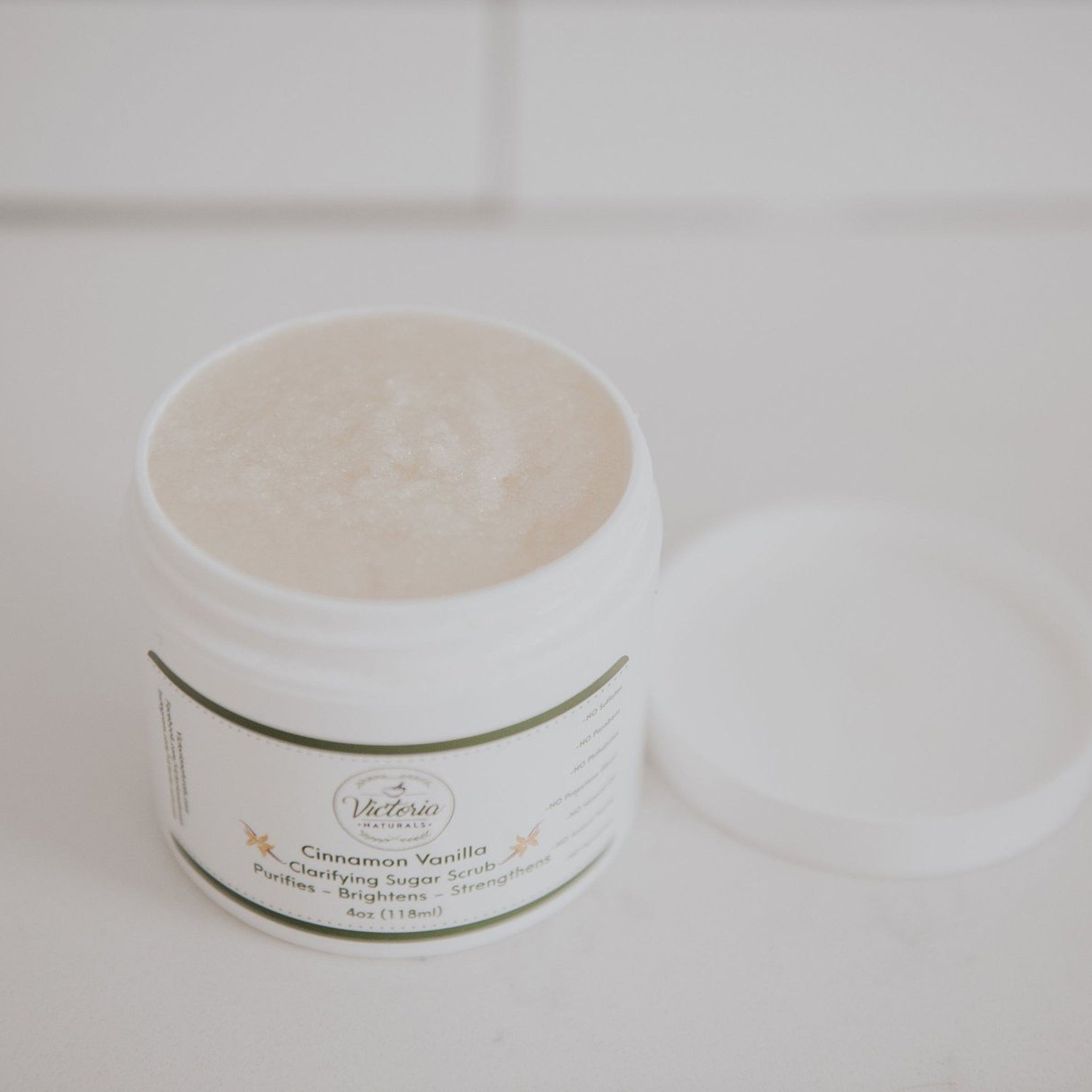 Sugar scrub jar, white plastic container, Victoria Naturals Cinnamon Vanilla label, open lid