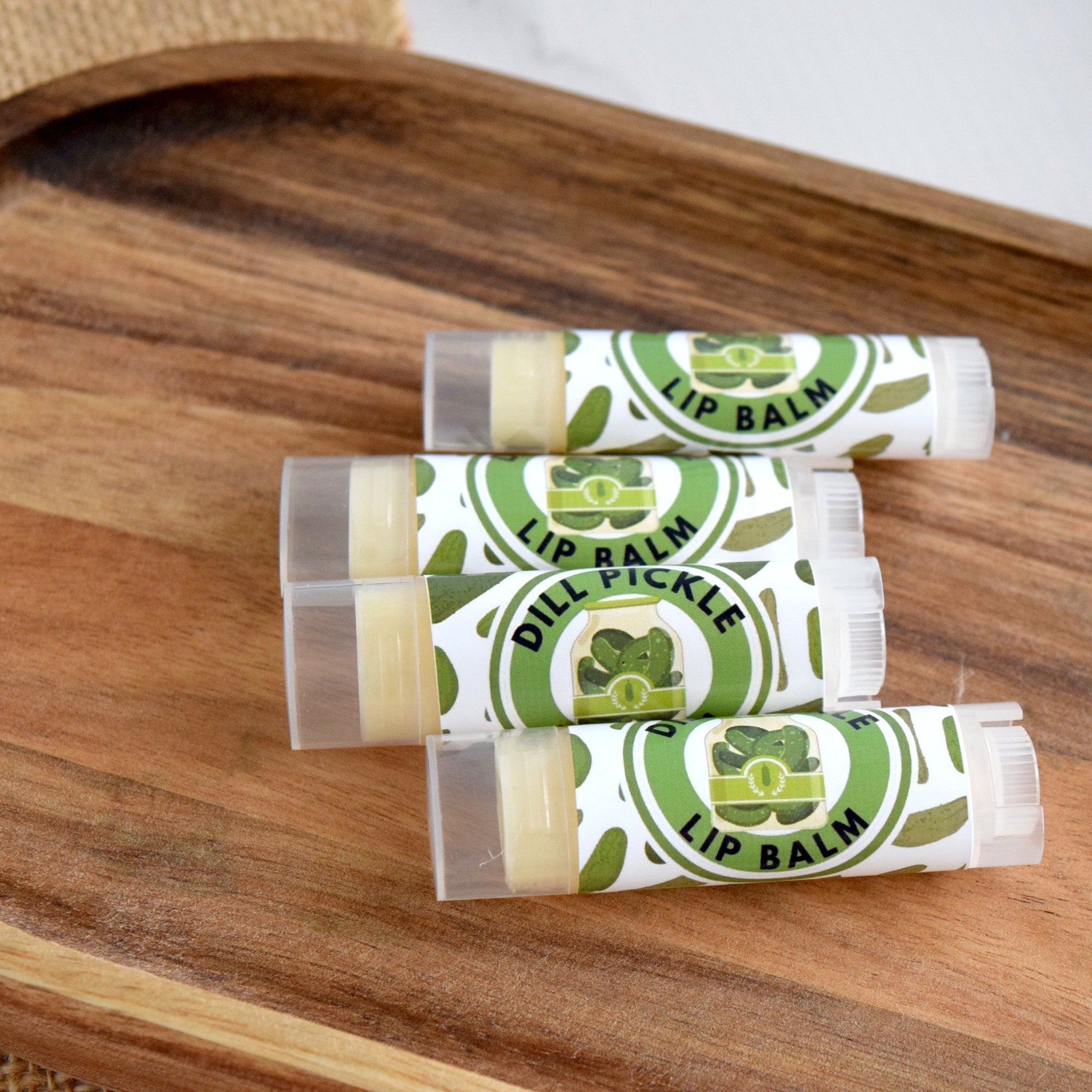 Lip balm tubes with green and white labels, on a wooden surface, "Dill Pickle" text visible