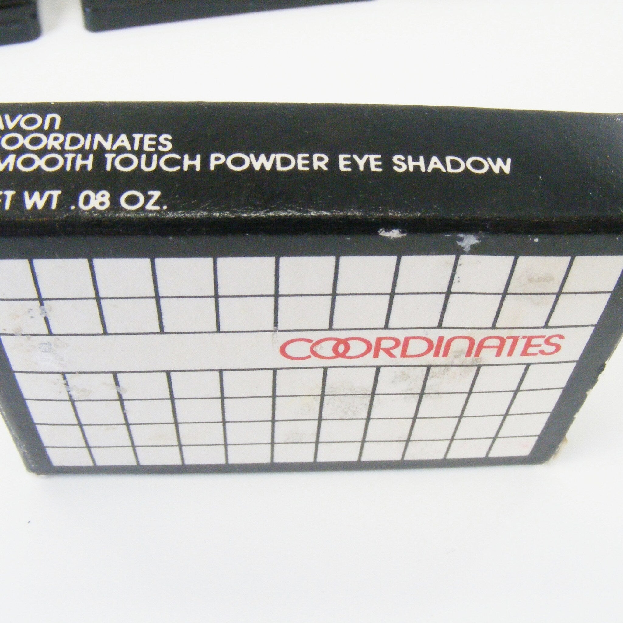 Eye shadow box, black with white grid, Avon Coordinates in red text on white background