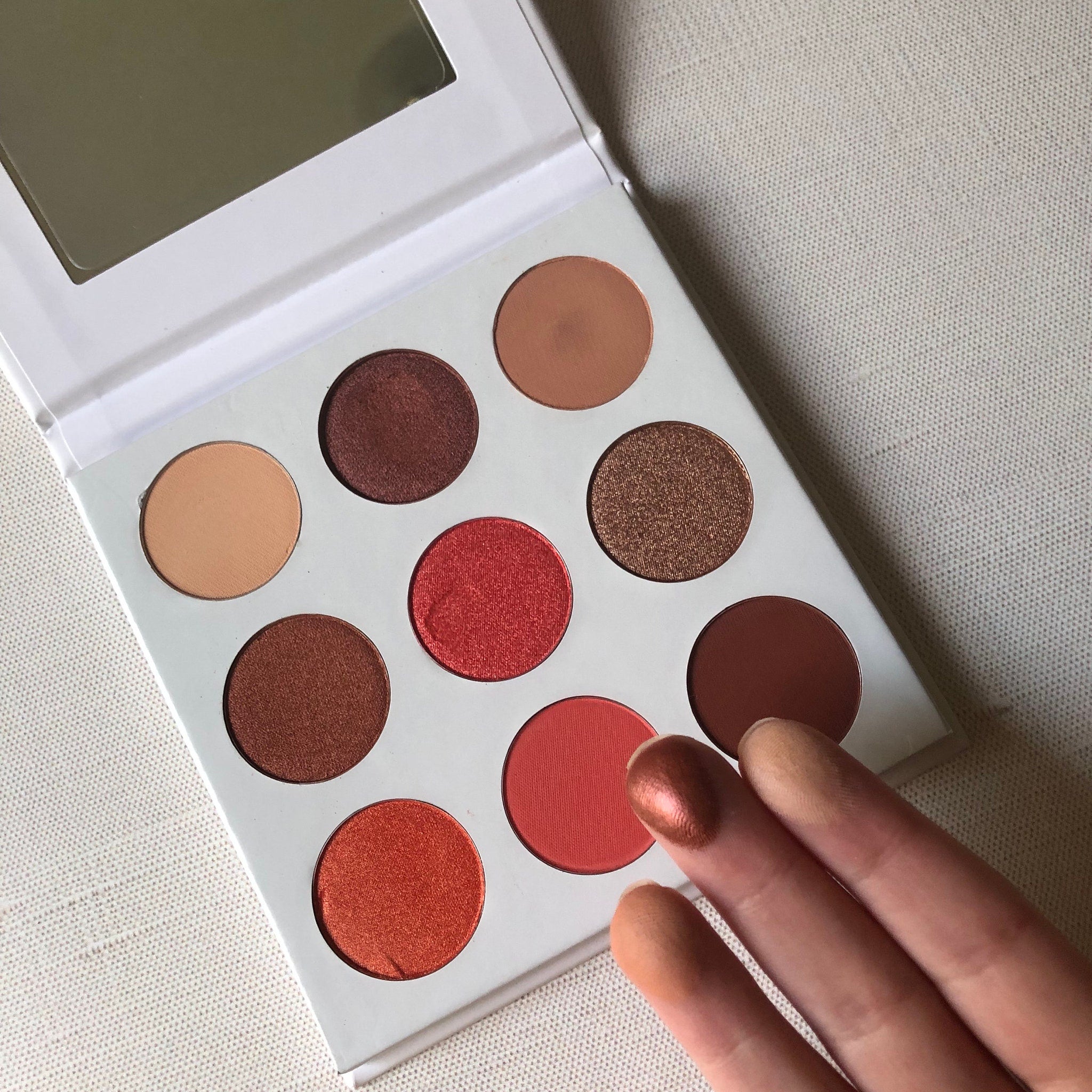 Close-up of the Red Daisies palette showing six vibrant matte and shimmer eyeshadows in warm red and pink tones
