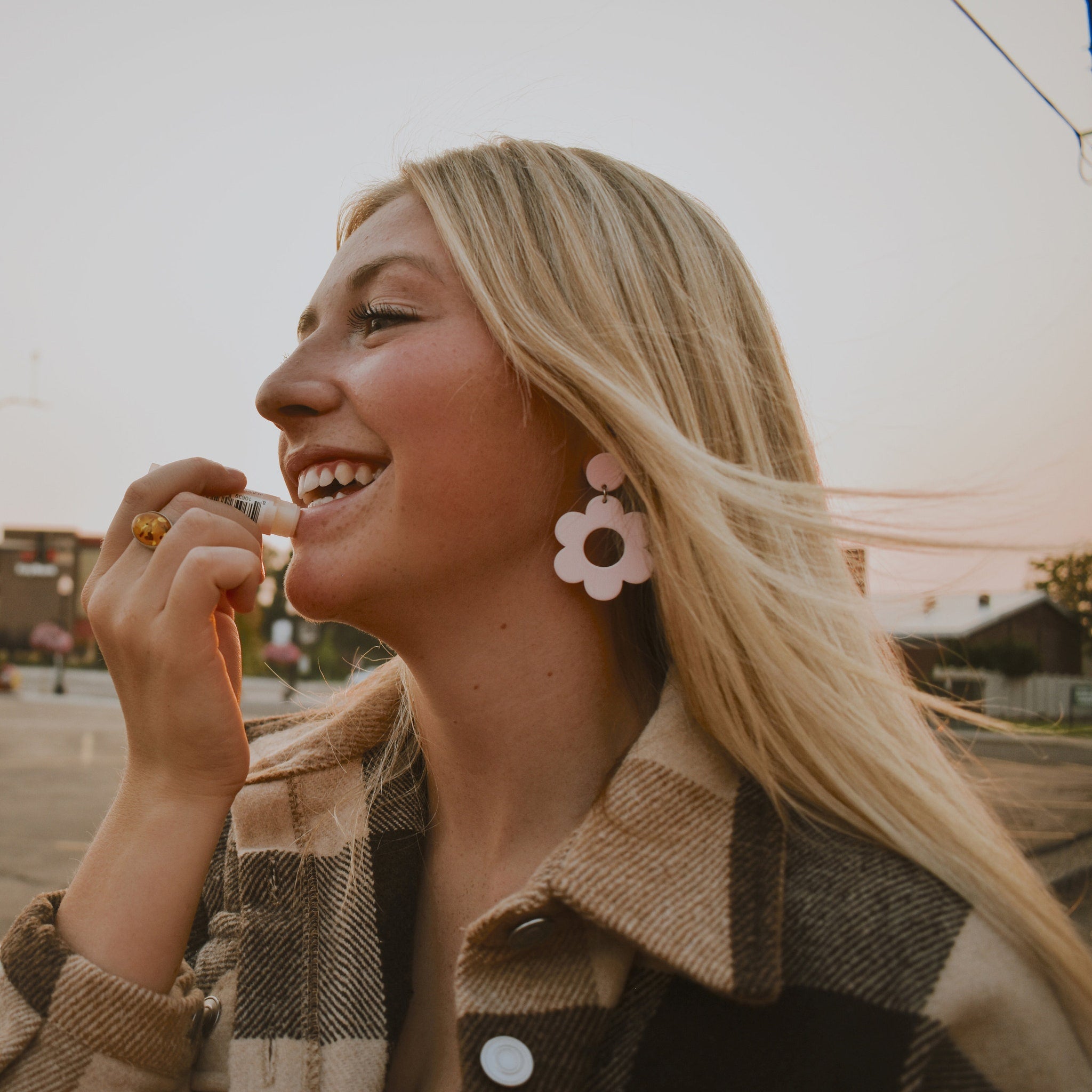 Lip balm tube held by woman with blonde hair and plaid shirt, smiling outdoors