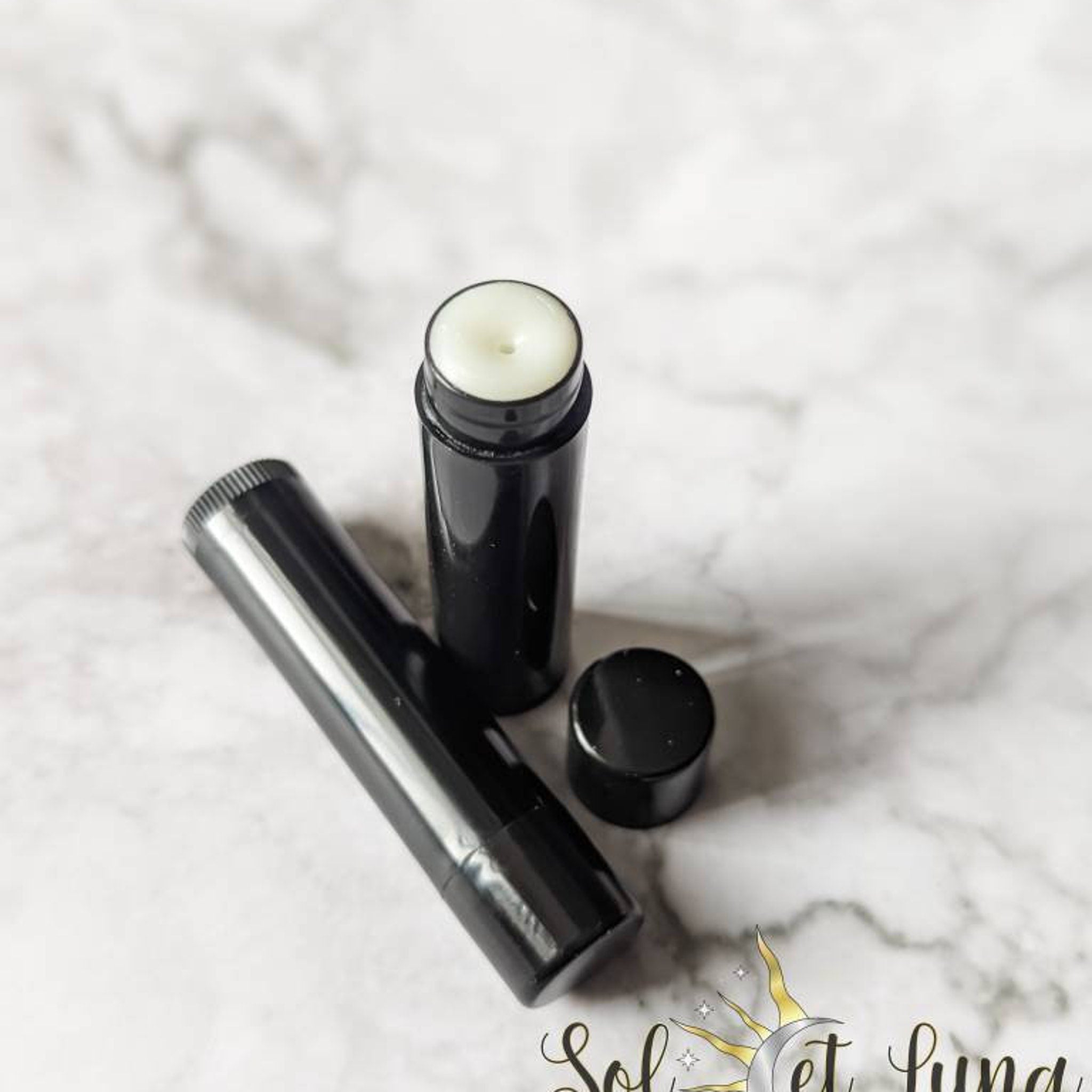 Lip balm in black tube with white balm visible, SOLETLUNA logo on surface
