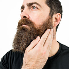 Beard, brown and gray hair, hand touching face, black shirt on man, looking up