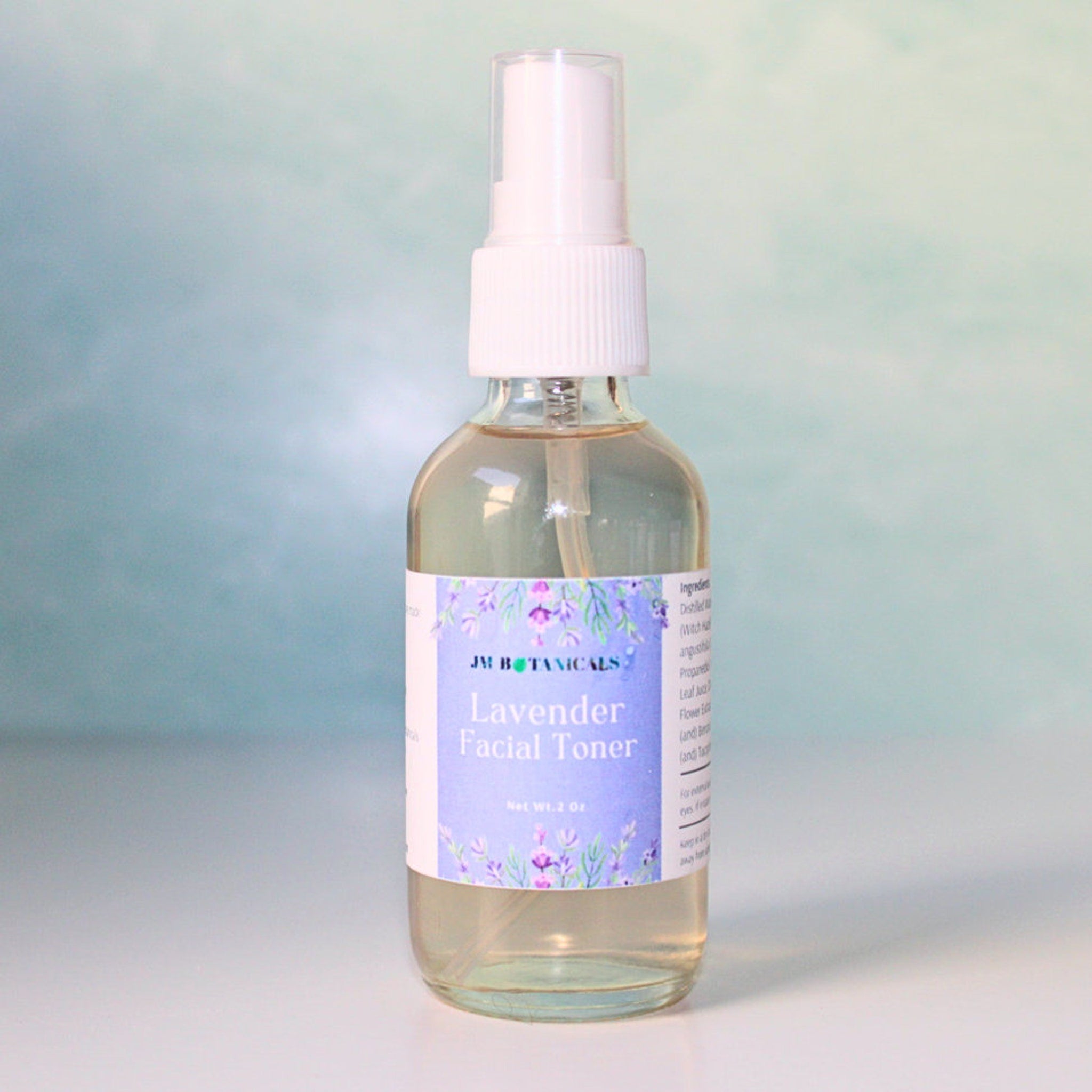 Lavender facial toner bottle with white spray top, clear glass, and floral label from JM Botanicals