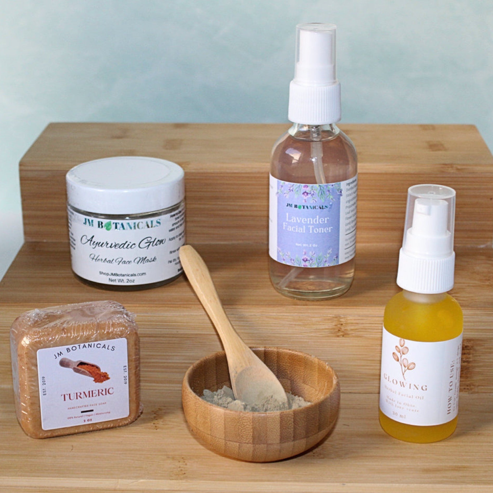 Face care products on wooden surface, including JM Botanicals Ayurvedic Glow jar, oil, and toner bottles