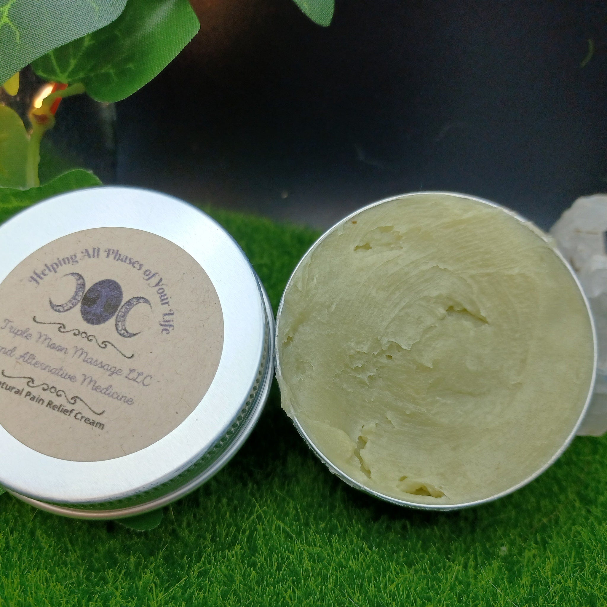 Pain relief cream, open silver tin with green cream, Triple Moon Massage LLC label visible