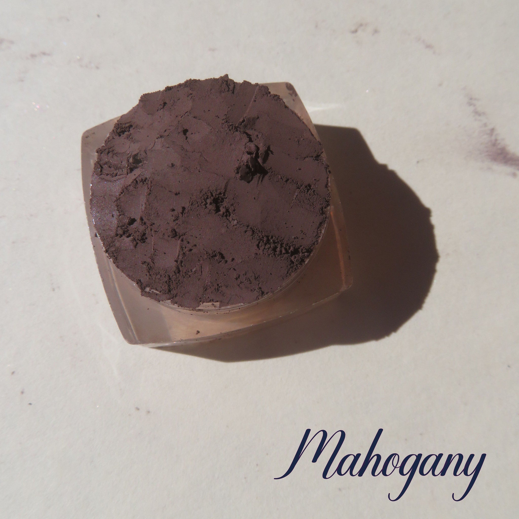 Side view of rich mahogany brown loose mineral eyeshadow powder spilling from container onto surface