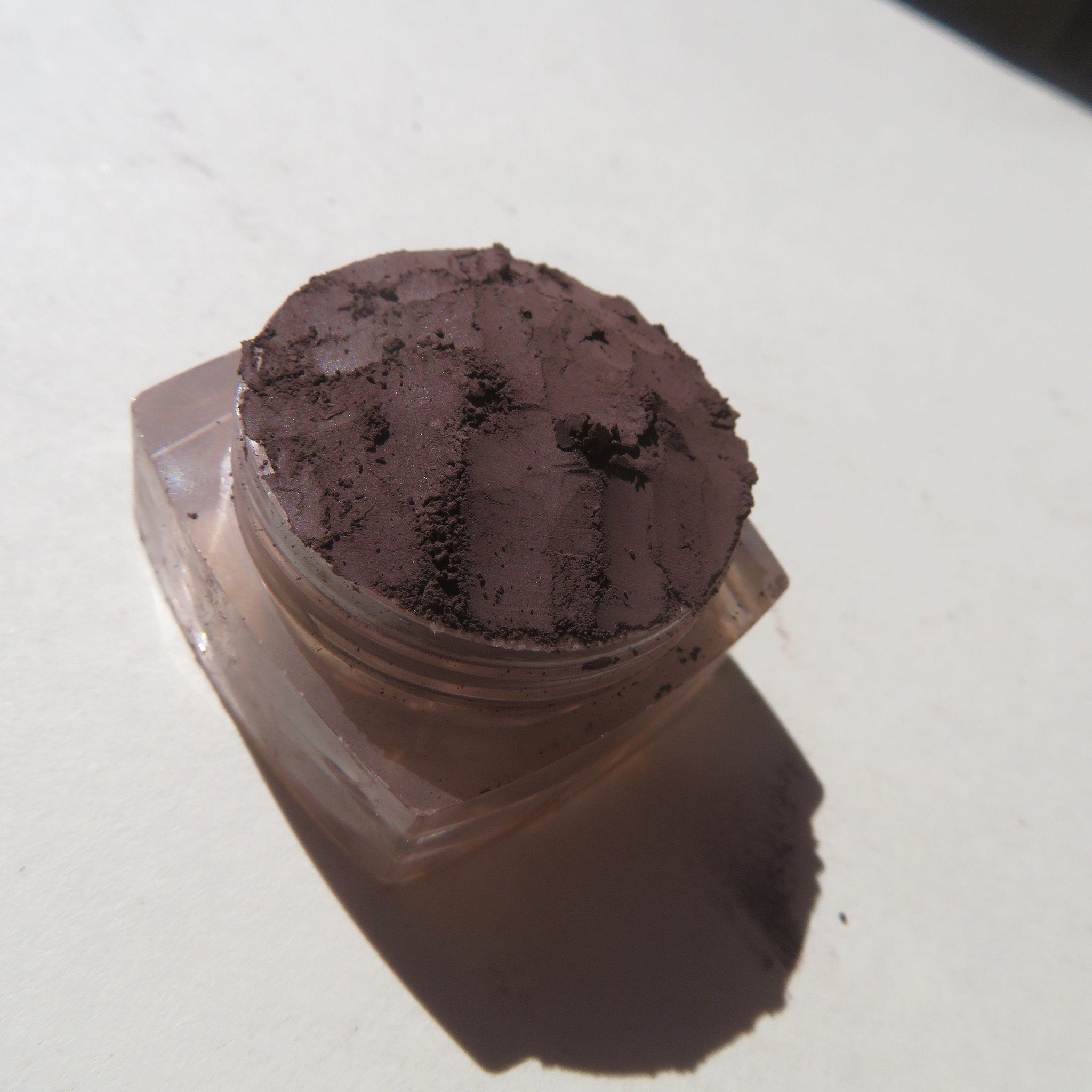 Dark brown loose mineral eyeshadow powder in a small black jar with silver lid and matte finish.