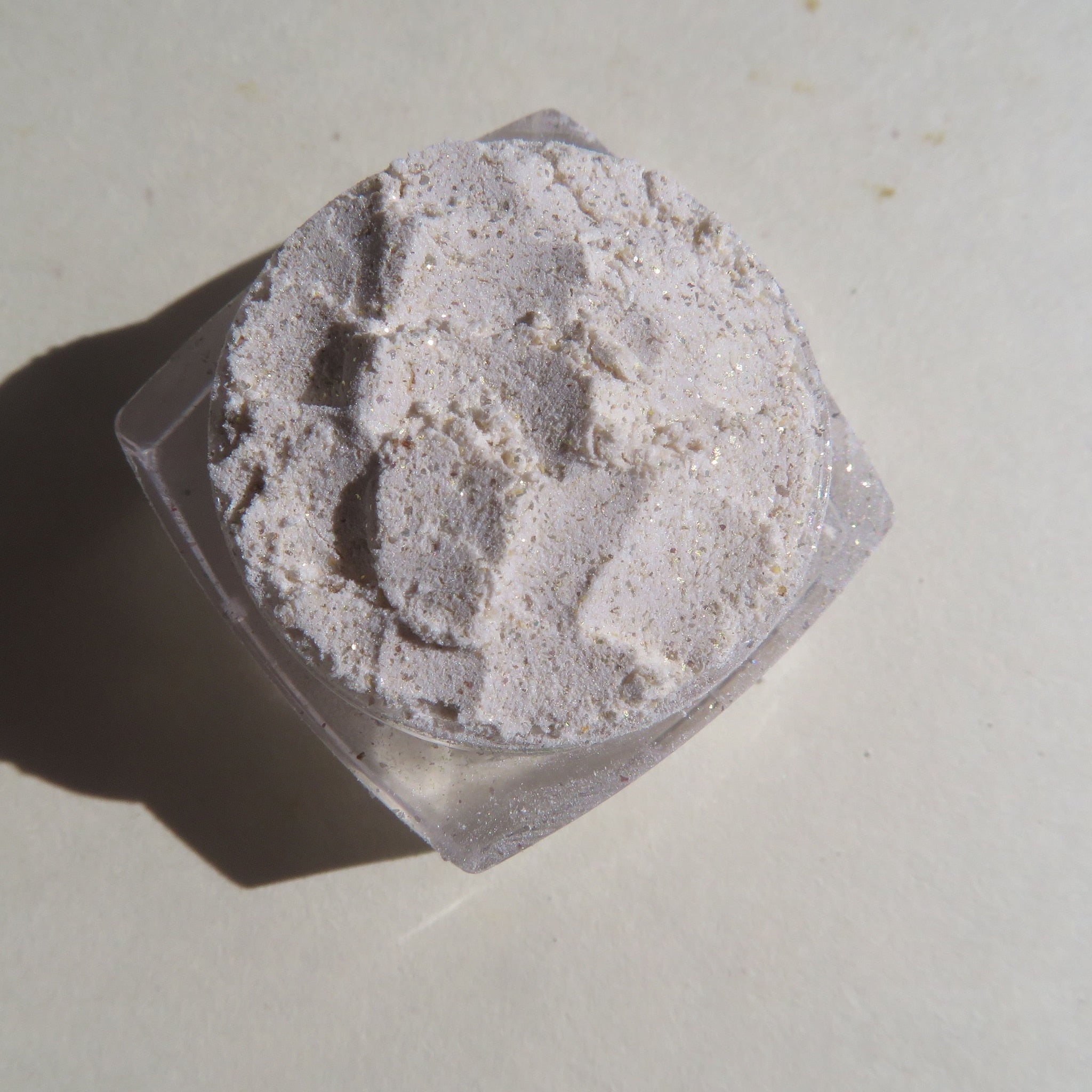 Powdered cosmetic product with white and gold glitter, in a clear plastic container