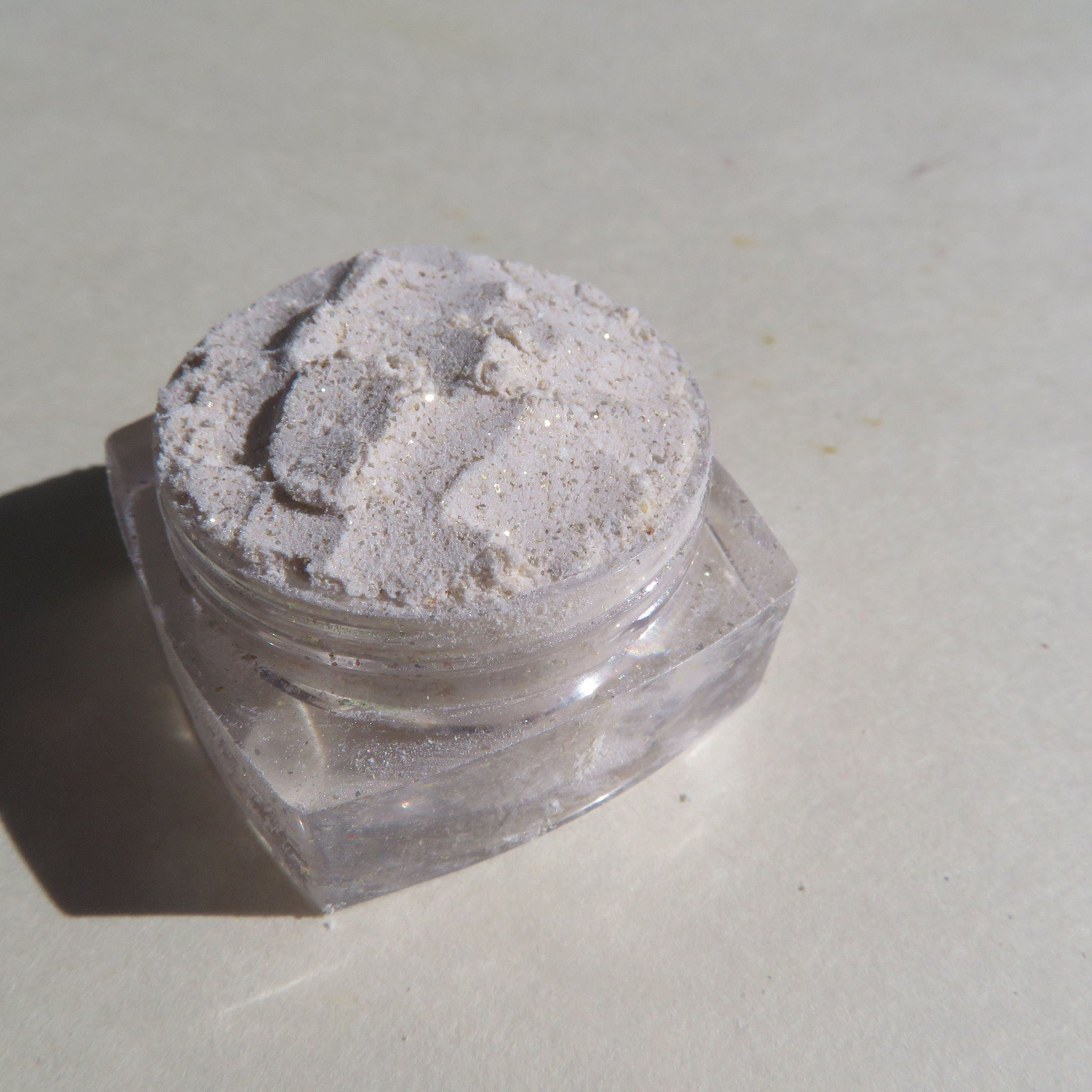 Powdered cosmetic with light beige color, glitter, and clear plastic jar
