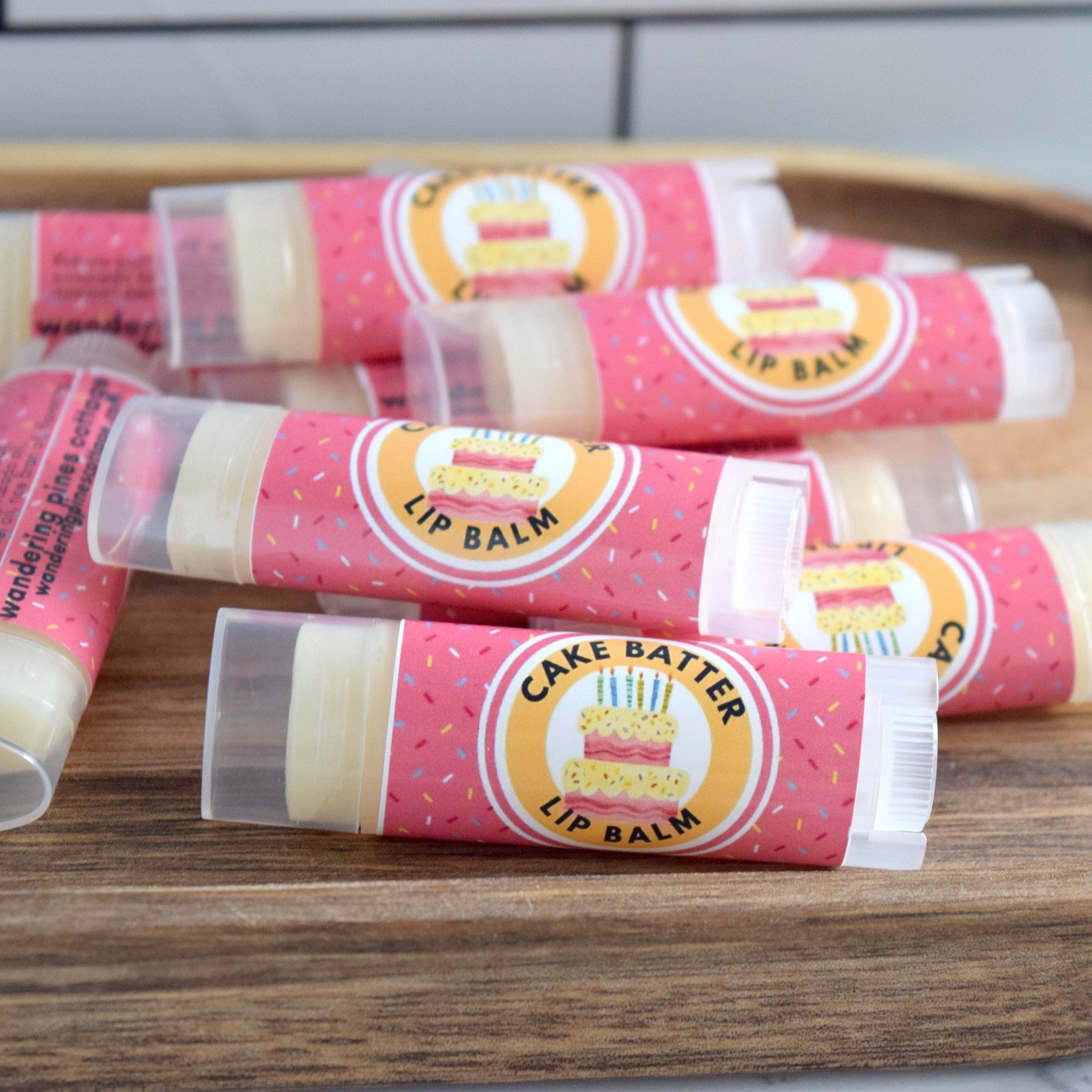 Lip balm tubes, pink with sprinkles, clear plastic cap, Cake Batter label on wooden surface