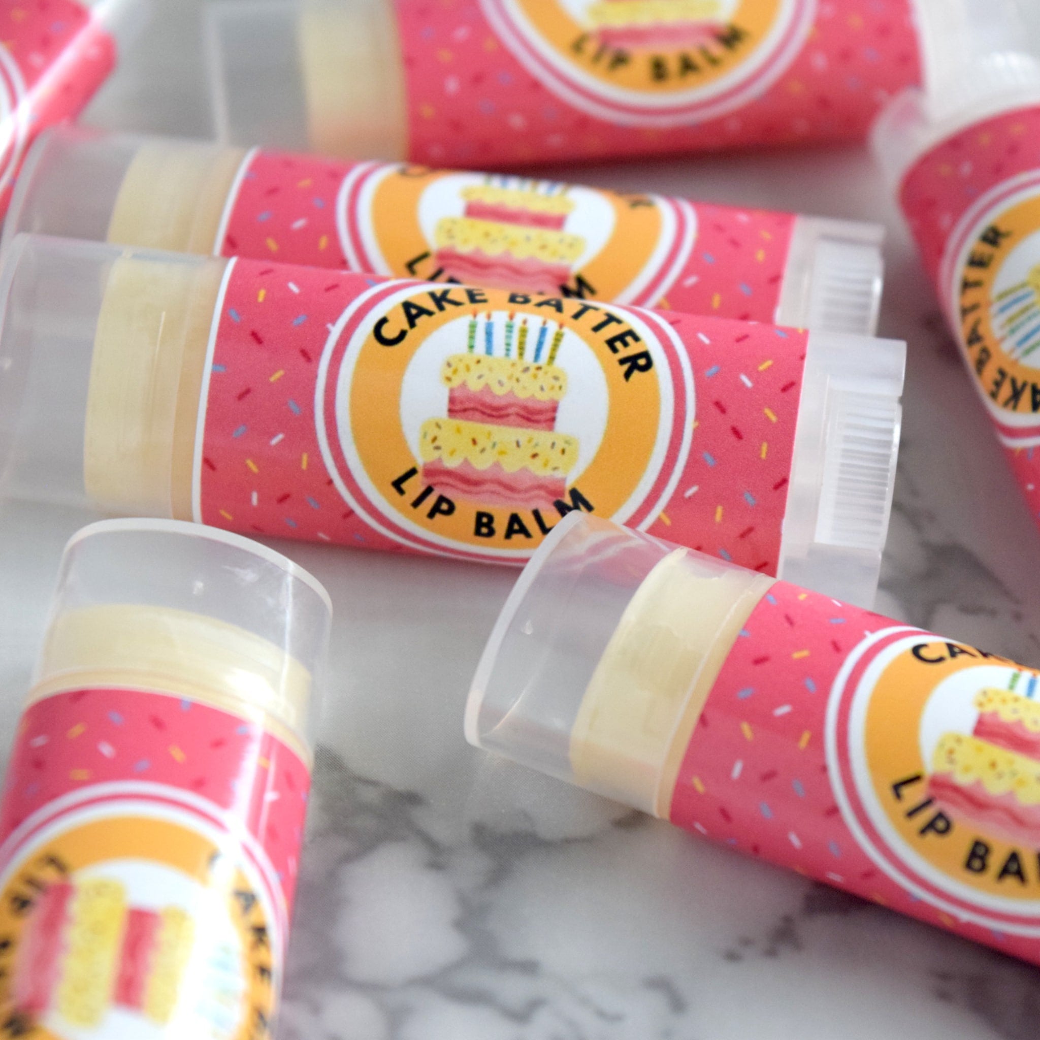 Lip balm tubes with pink patterned labels and clear plastic caps, Cake Batter text visible