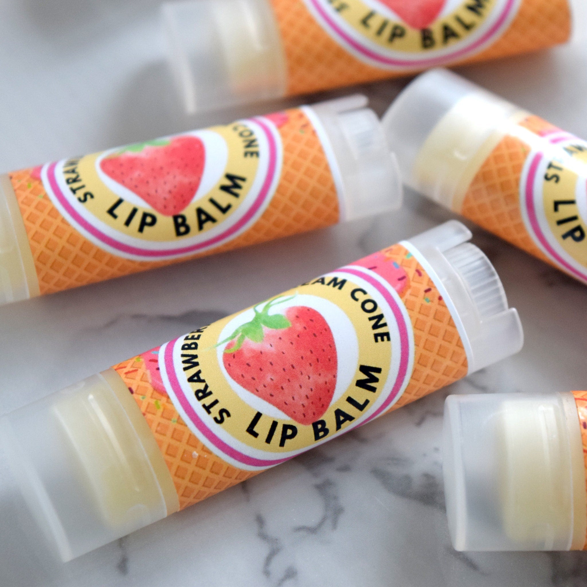 Lip balm tubes with strawberry design, orange waffle pattern, and clear plastic cap