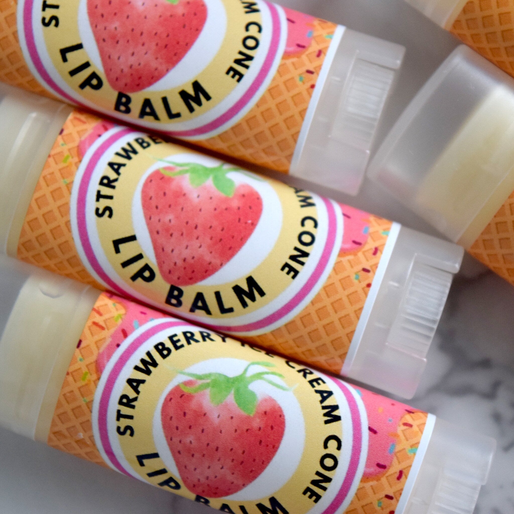 Lip balm tubes with strawberry and ice cream cone design, pink and yellow labels, clear plastic caps