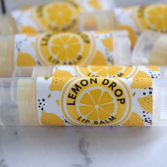 Lip balm tubes with yellow and white labels, "Lemon Drop" text, and clear plastic containers