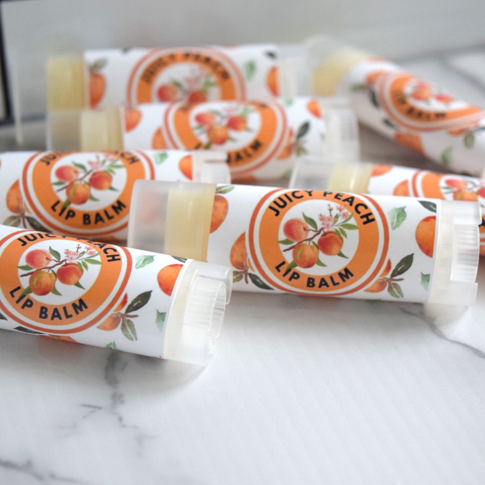 Lip balm tubes with white and orange labels, peach illustration, and "Juicy Peach Lip Balm" text.