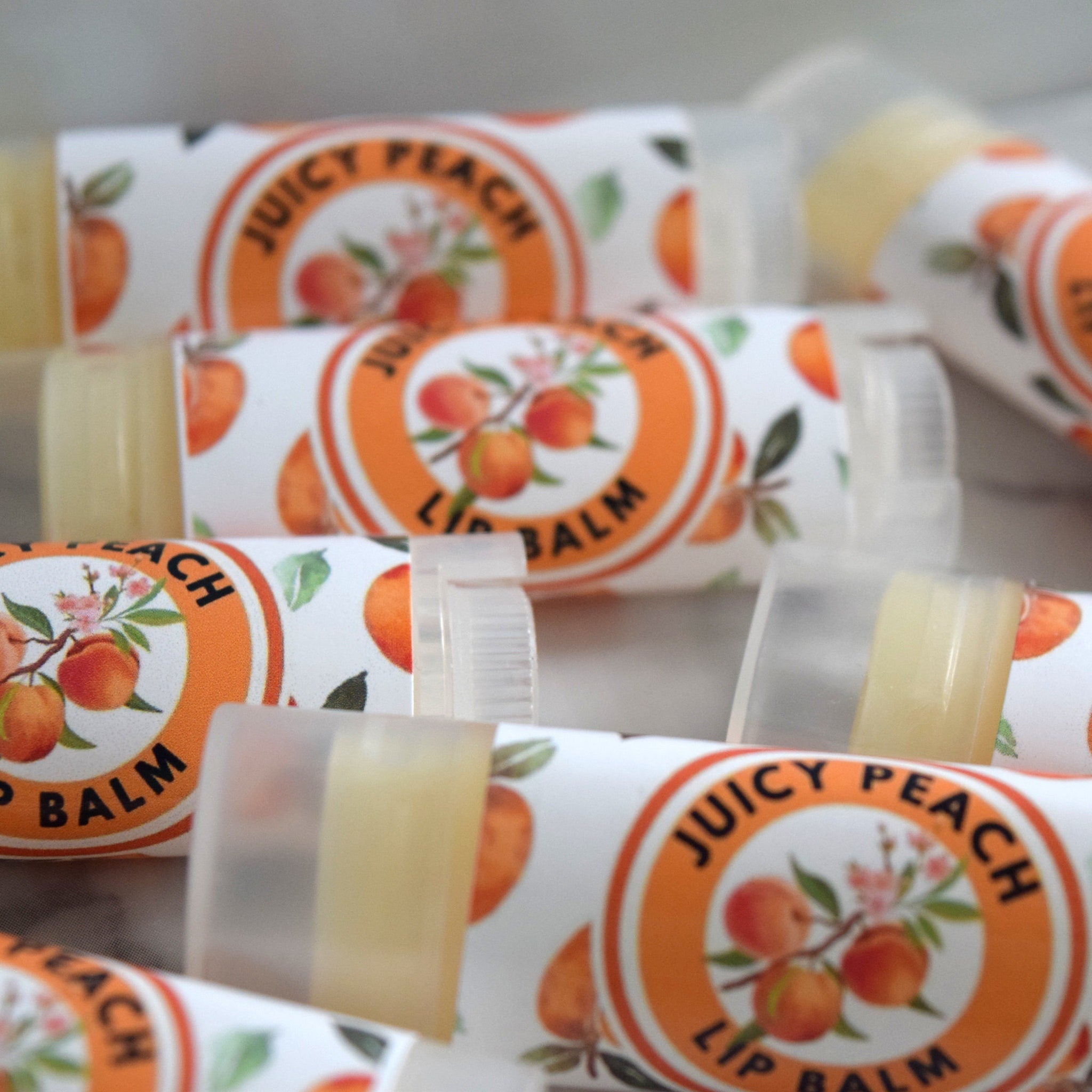 Lip balm tubes with white and orange labels, clear plastic caps, and "Juicy Peach" text