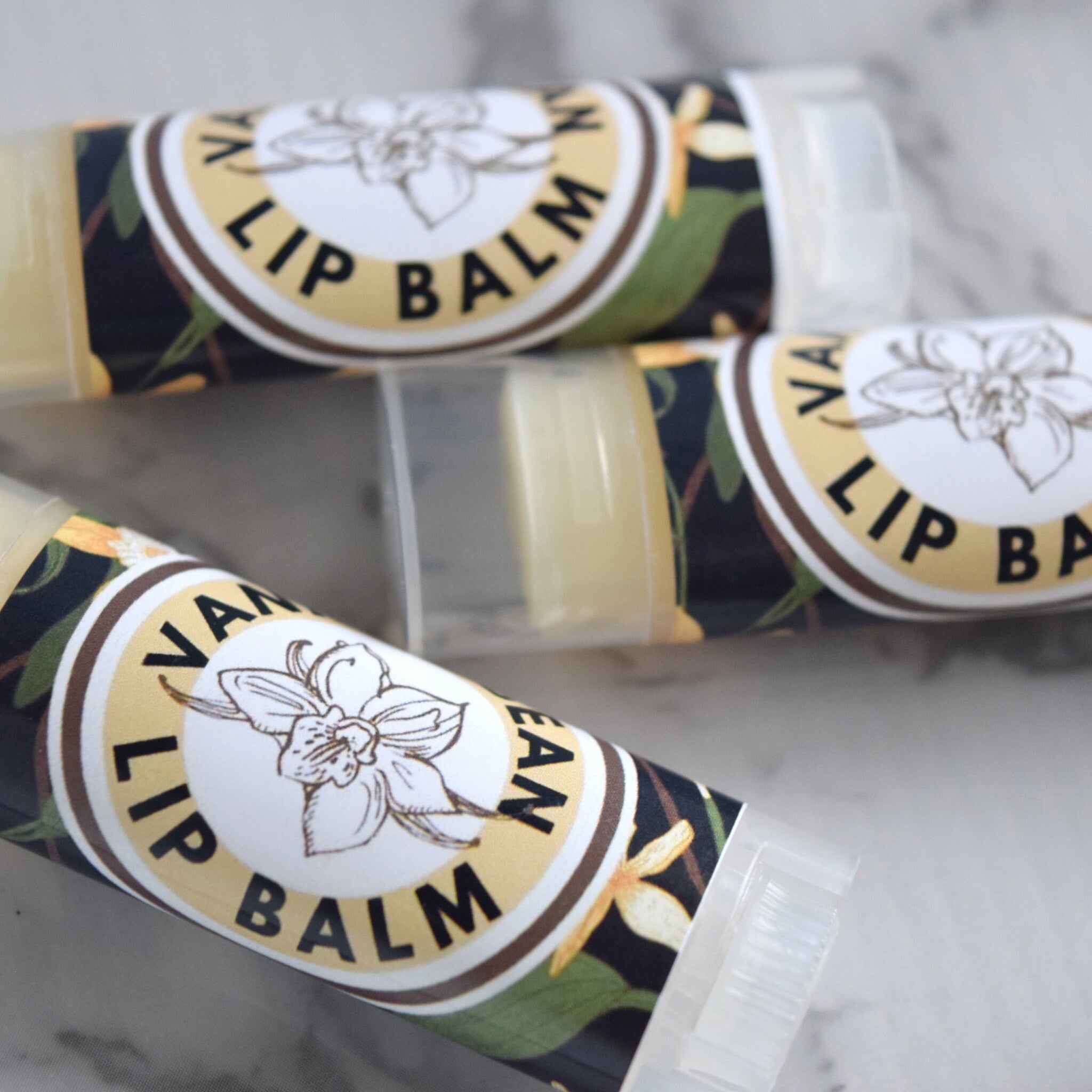 Lip balm tubes with vanilla label, floral pattern, and clear plastic container