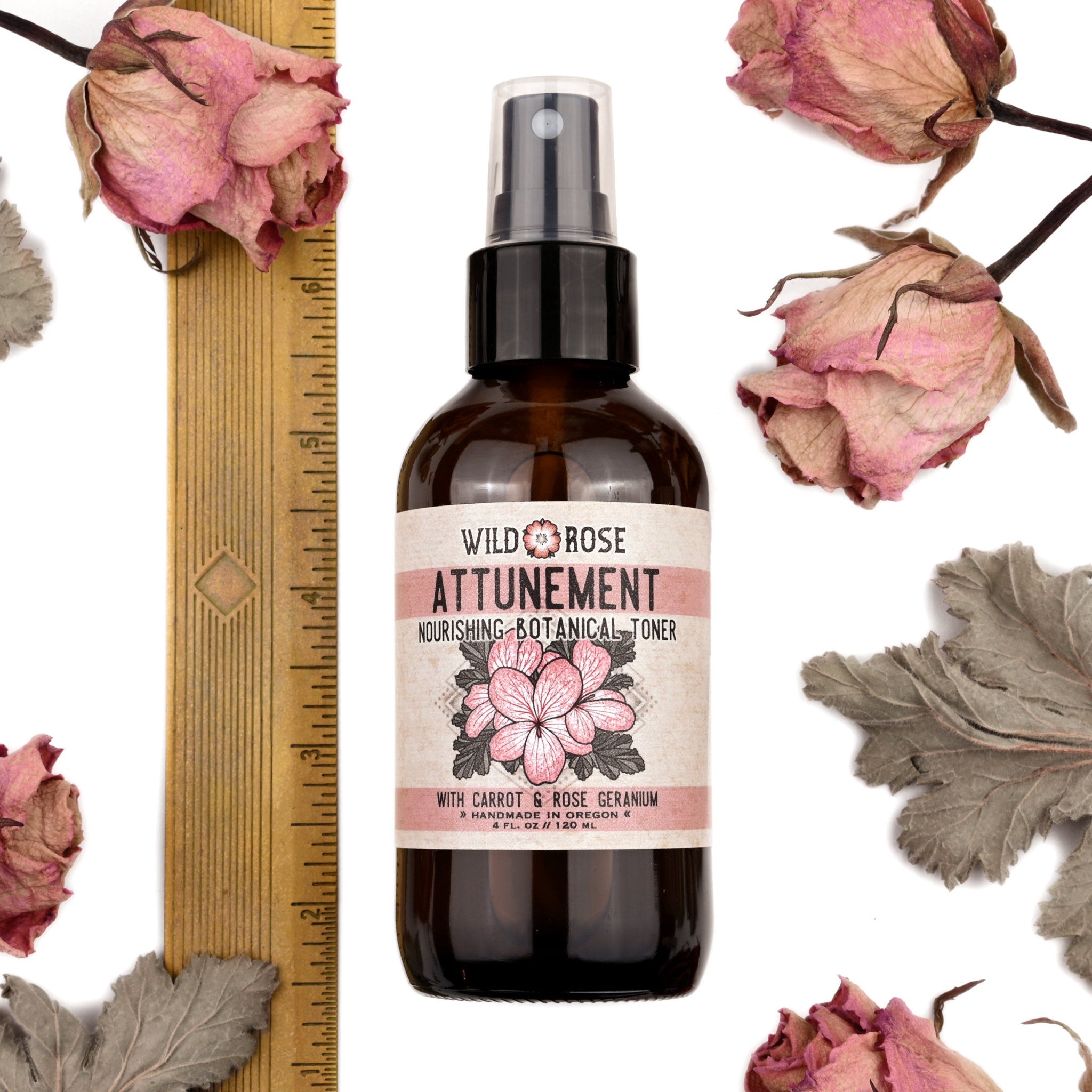 Toner bottle with brown glass, black cap, and Wild Rose Attunement label with pink text and flower design surrounded by dried flowers and a ruler