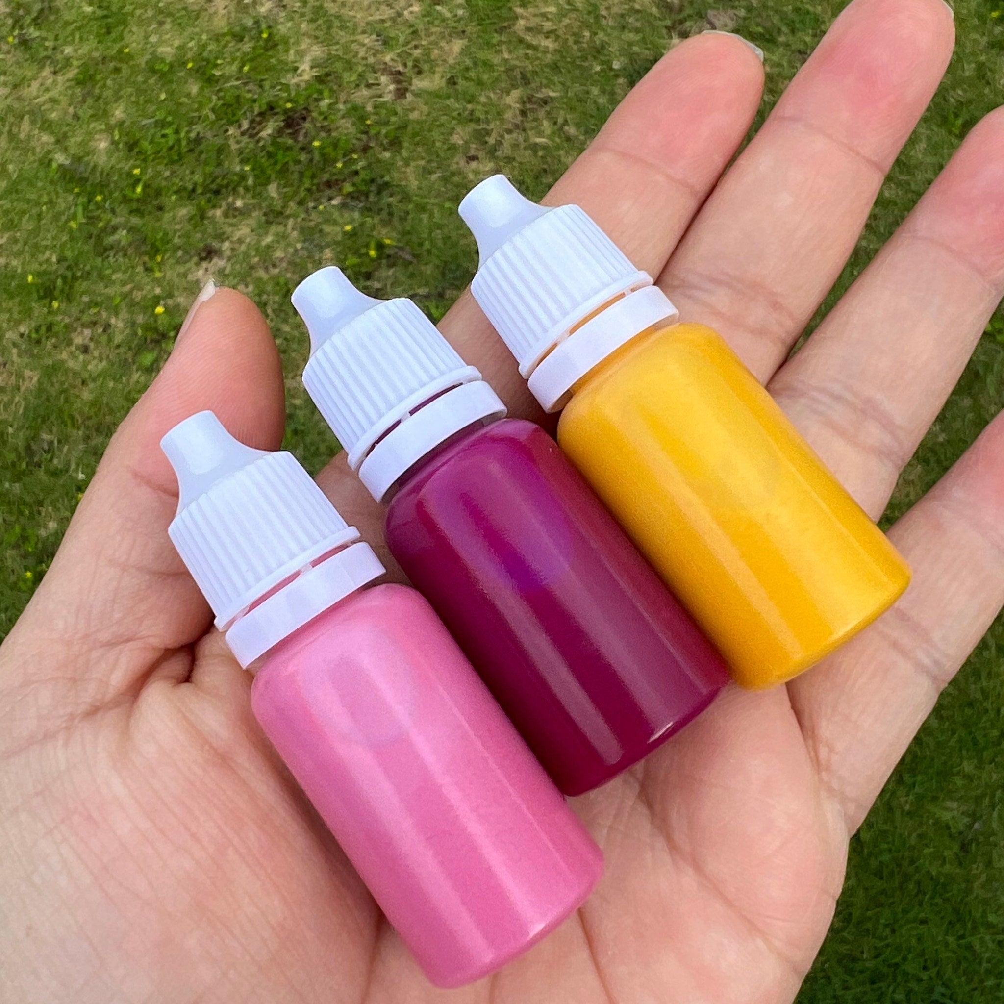 Dropper bottles in pink, purple, and yellow with white caps held in hand