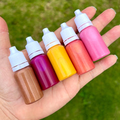 Lip liquids in various colors, held in hand, with white caps and clear bottles