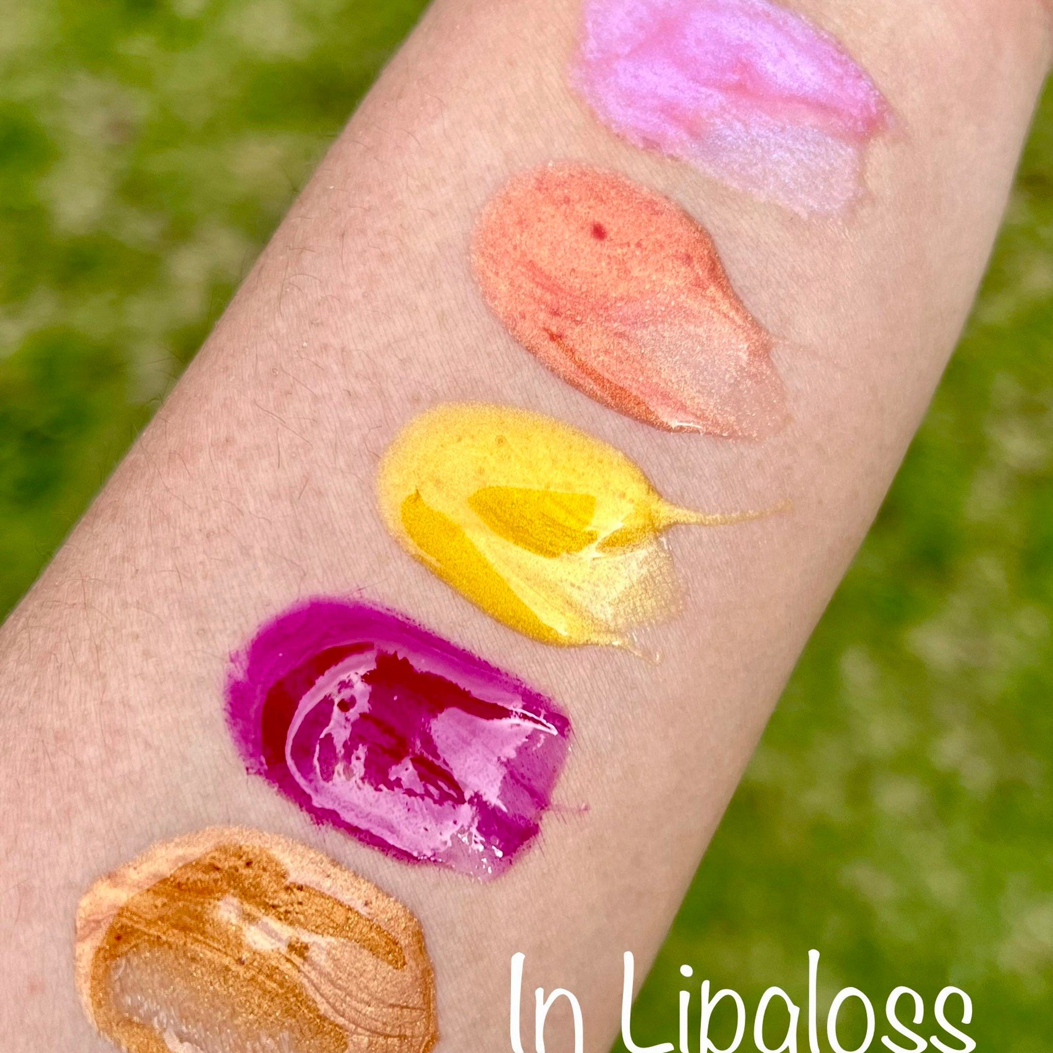 Lip gloss swatches in pink, orange, yellow, purple, and gold on arm, In Lipgloss text visible