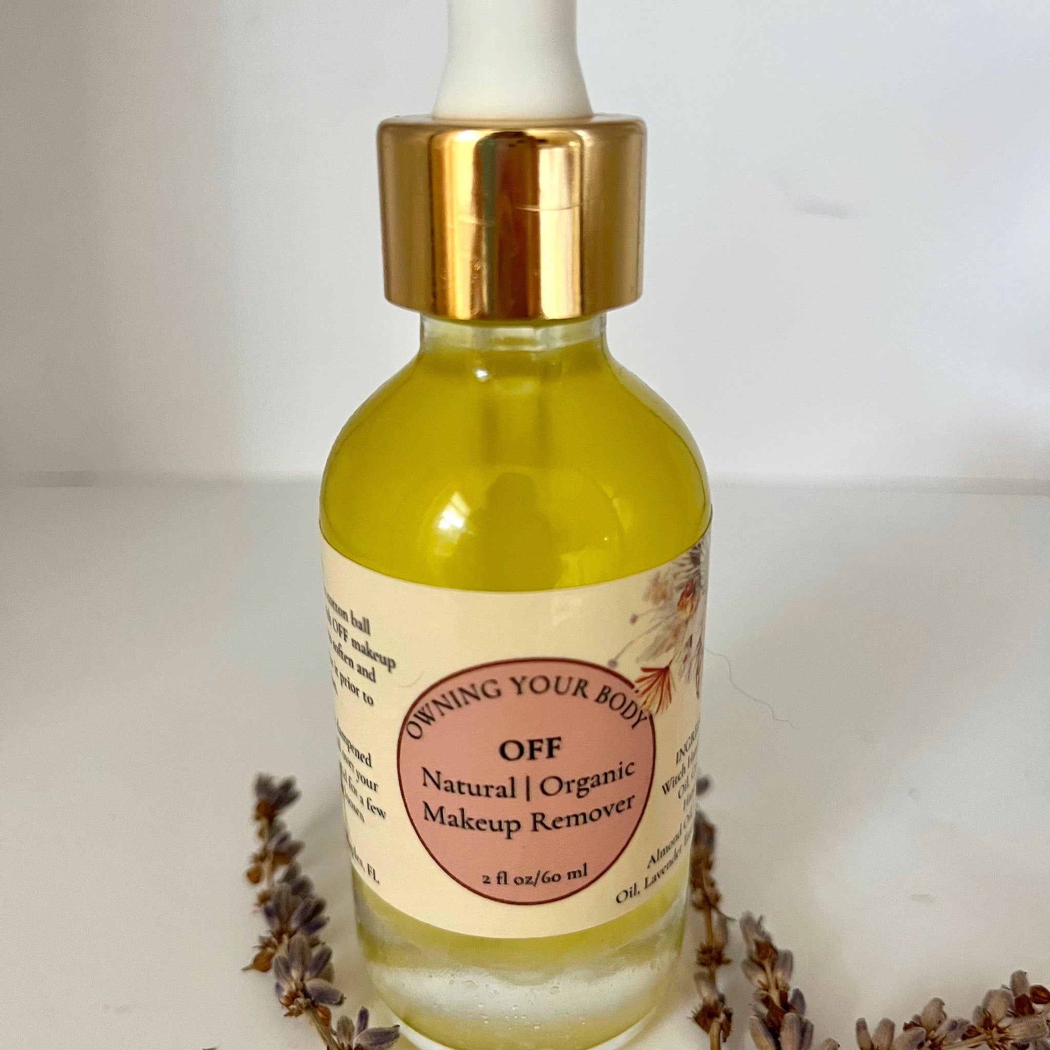 Makeup remover bottle with gold cap, yellow liquid, and "OFF" label with floral accents on white background