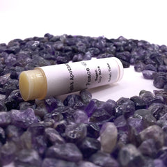 Vegan lip balm tube with white label, yellow balm, and Aura Light Apothecary text, surrounded by purple stones