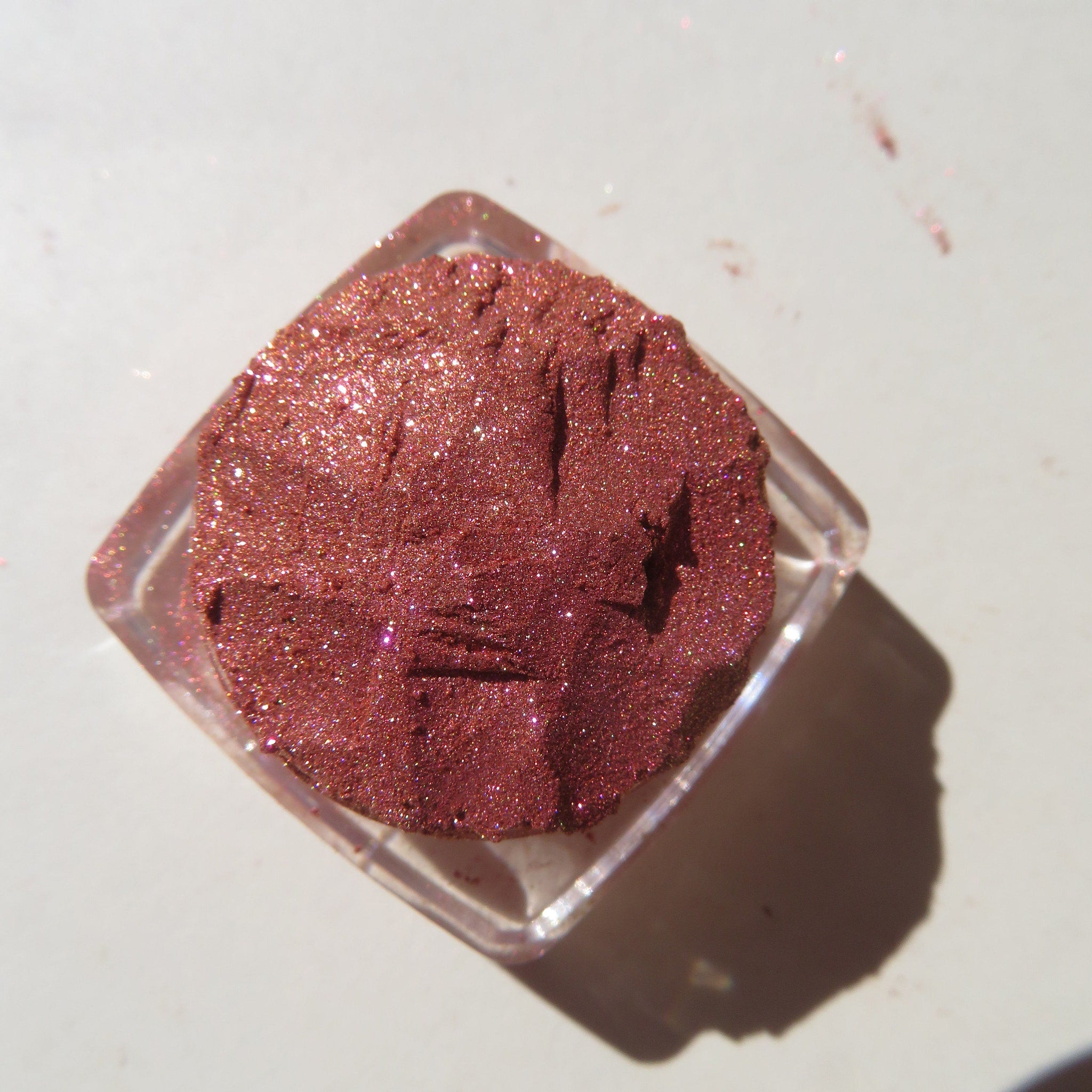 Close-up of shimmering loose pigment in orange-pink-gold tones with metallic finish, vegan mineral eye shadow