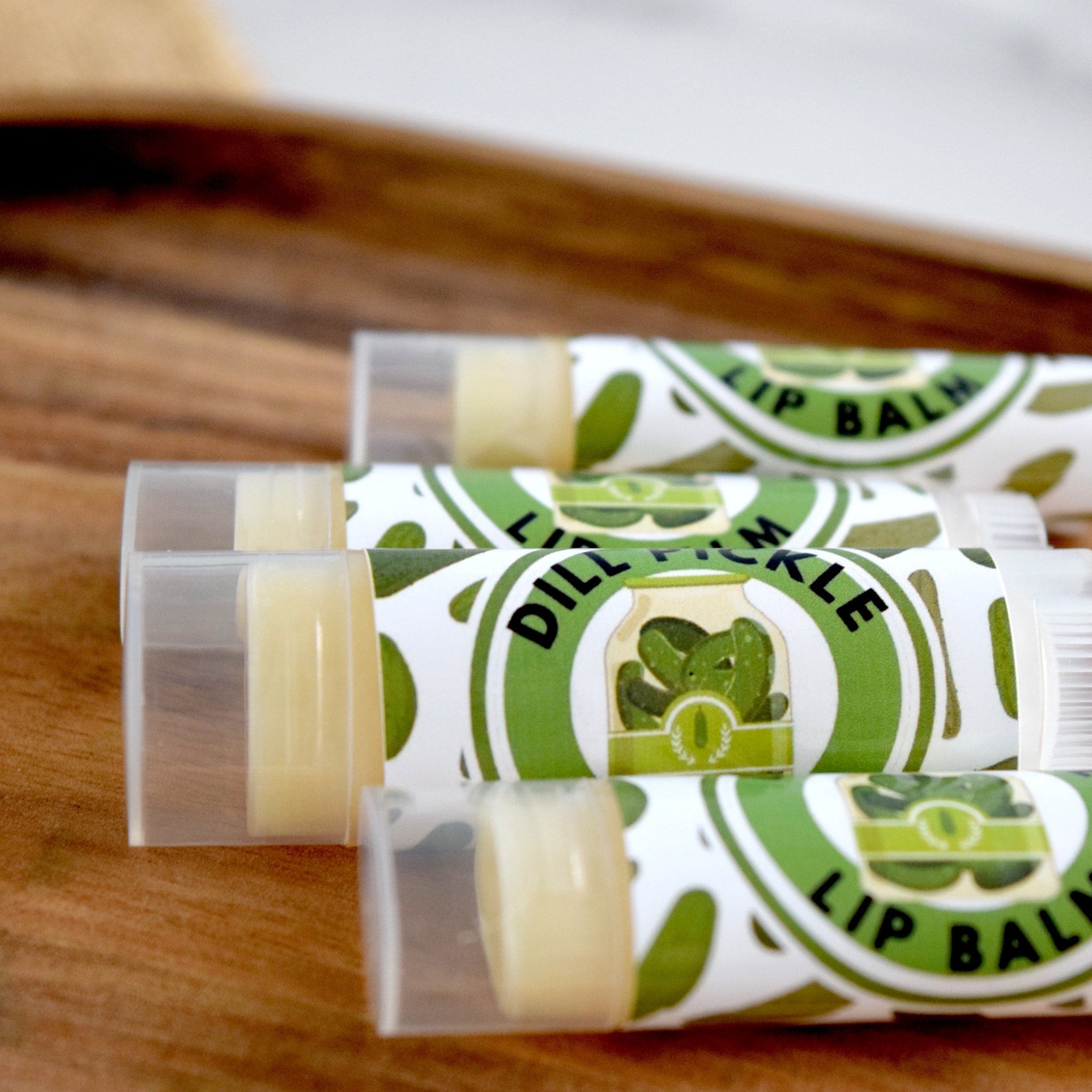 Lip balm tubes with green and white labels, clear caps, and yellow balm inside, on wood surface