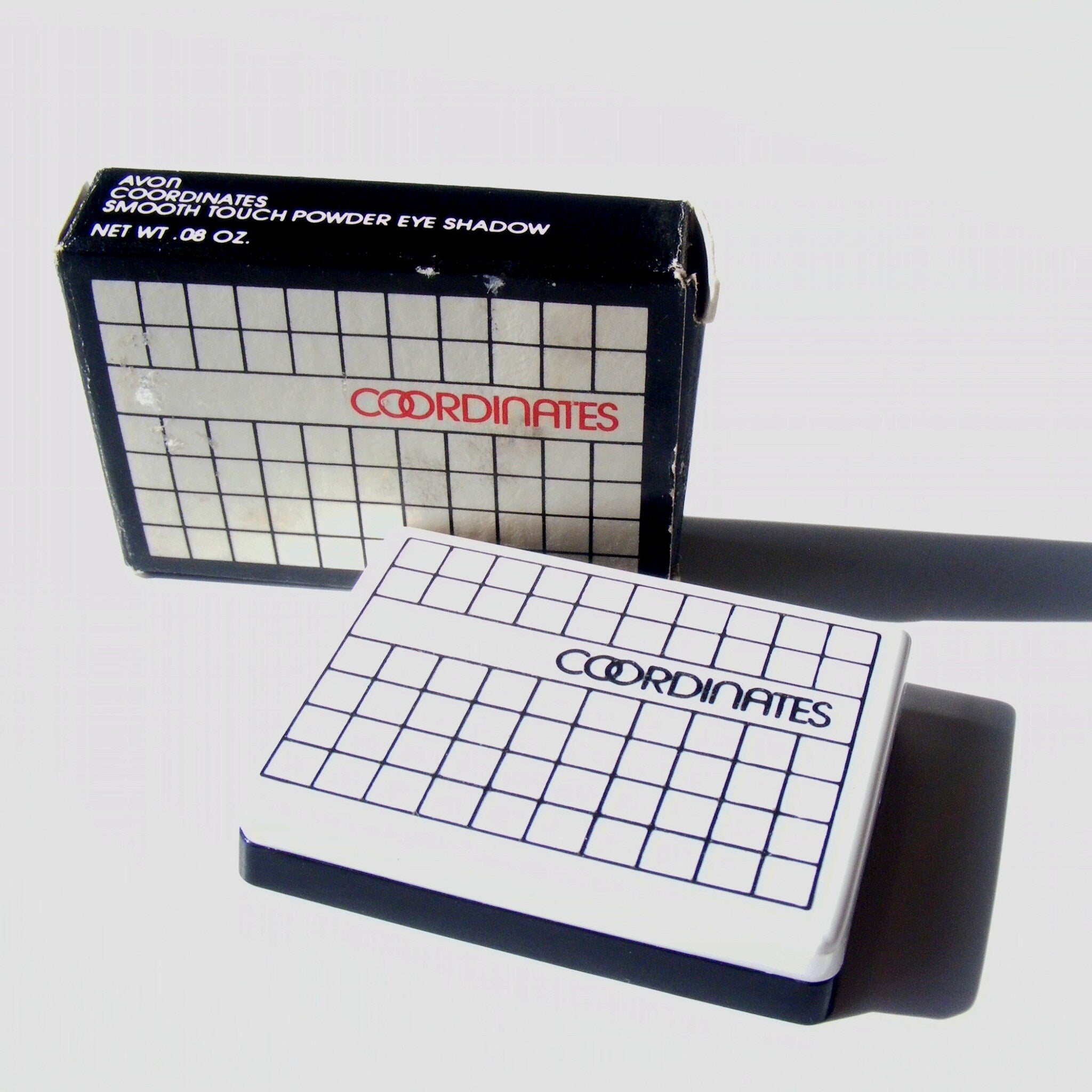 Eye shadow compacts, white grid pattern, black border, Avon Coordinates branding visible