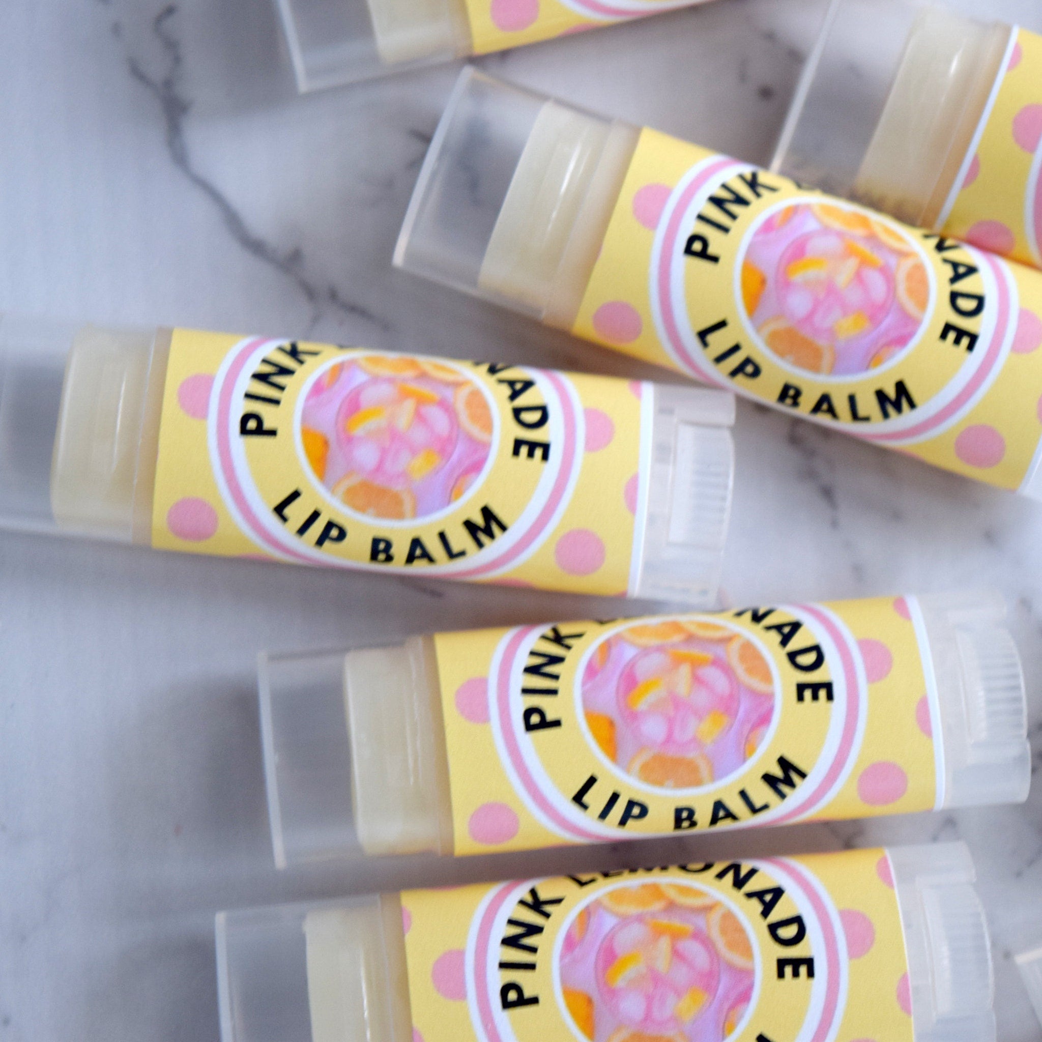 Lip balm tubes with yellow and pink labels, clear plastic caps, and text "Pink Lemonade