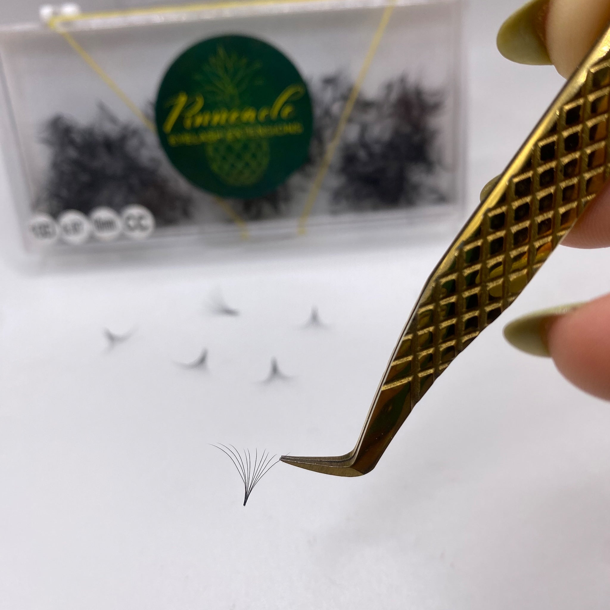 Eyelash extensions with black strands held by gold tweezers on white surface